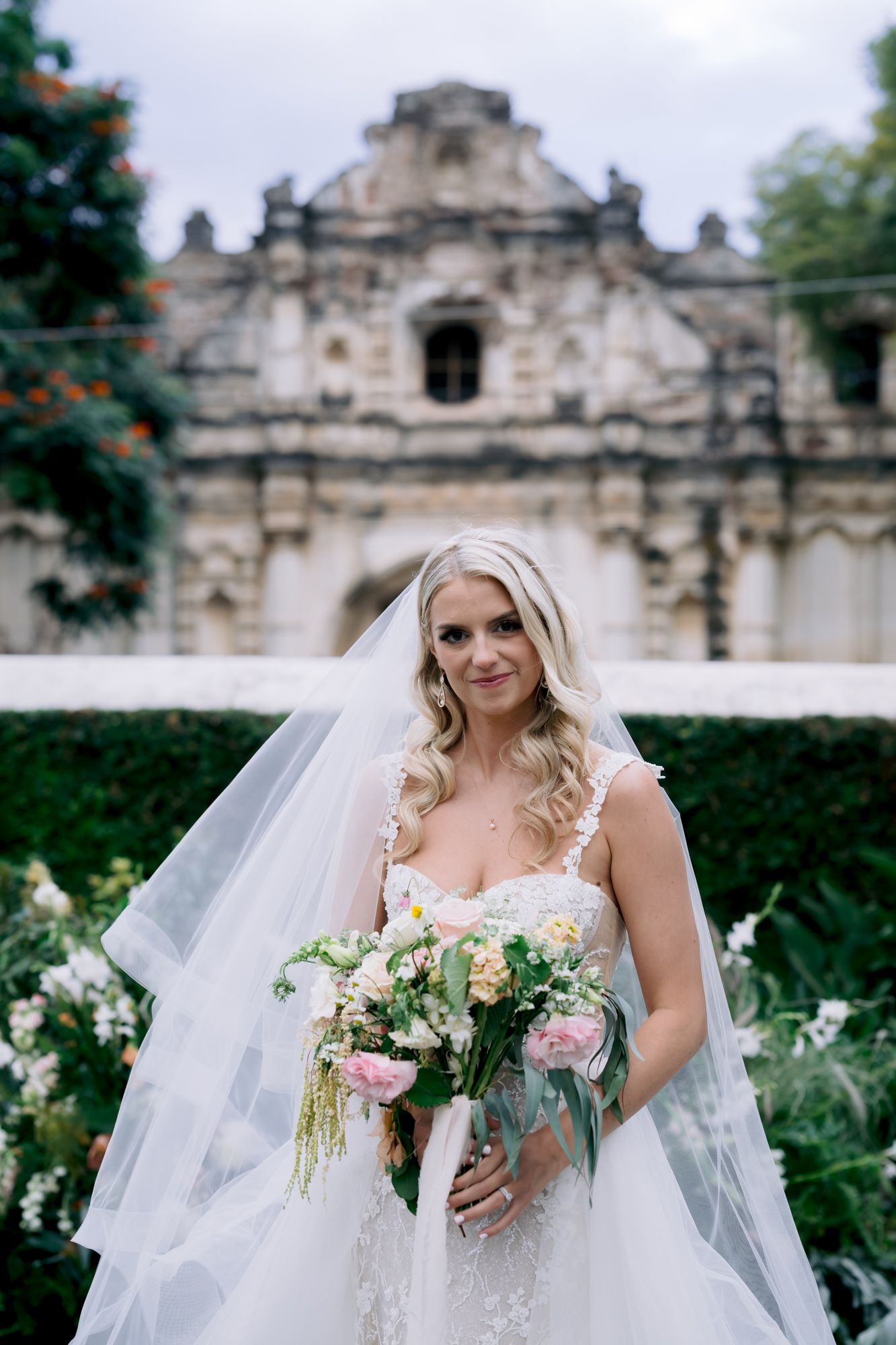 An elegant bridal portrait in front of a historic Spanish colonial church with beautiful garden surroundings.