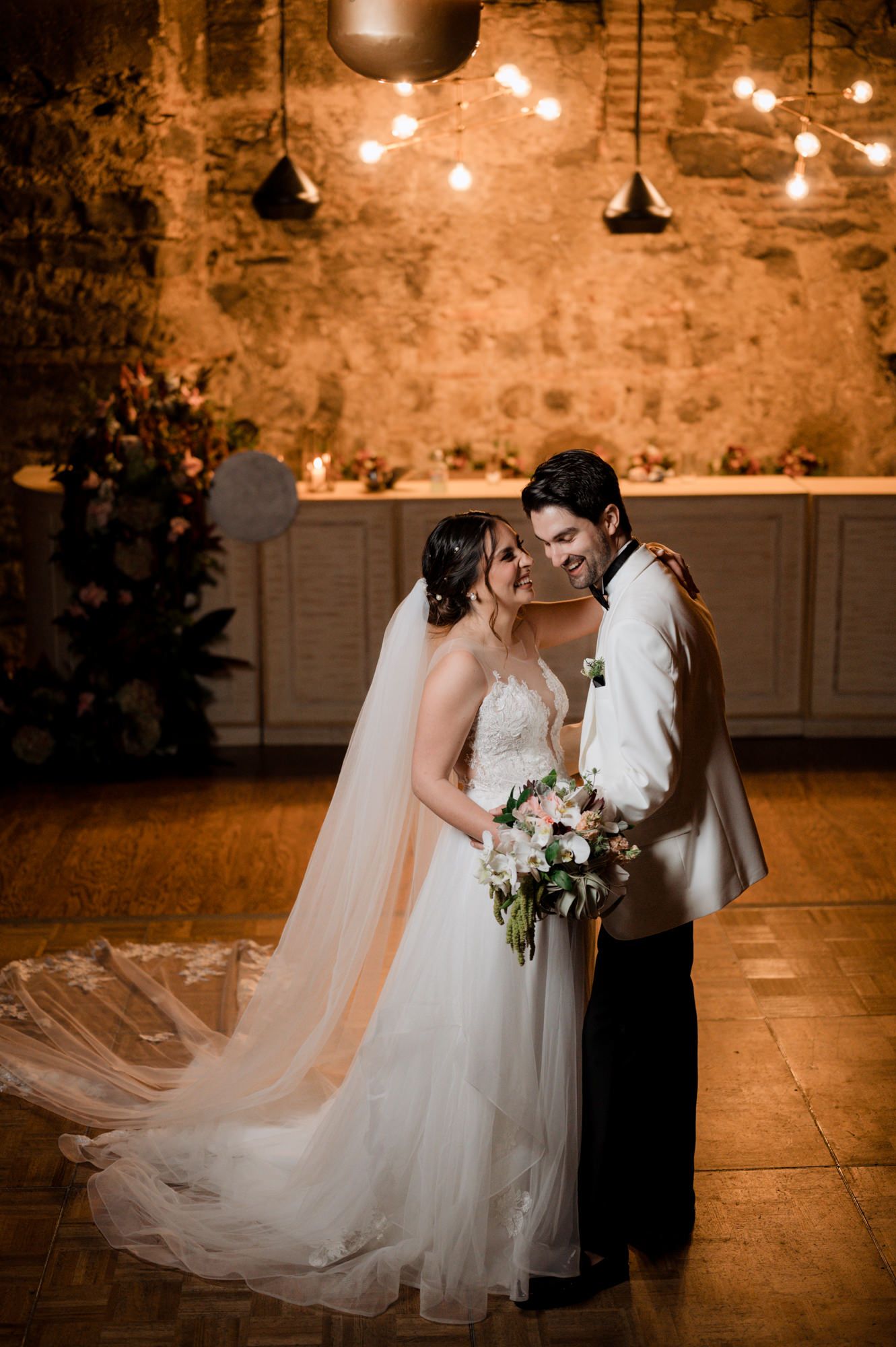 Romantic wedding portrait with string lights and rustic brick wall backdrop.