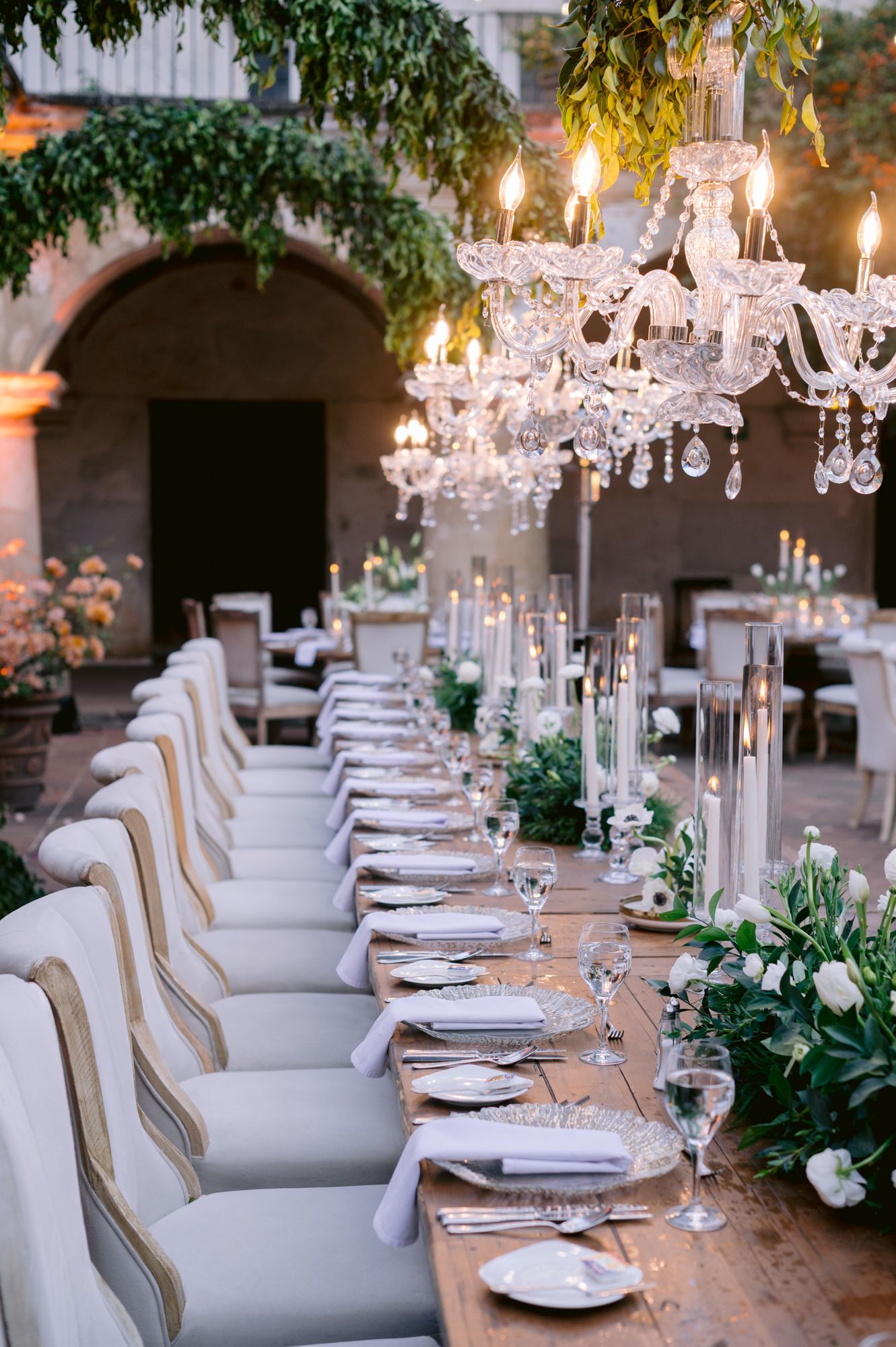 Luxurious wedding table setting with crystal chandelier and white floral arrangements.