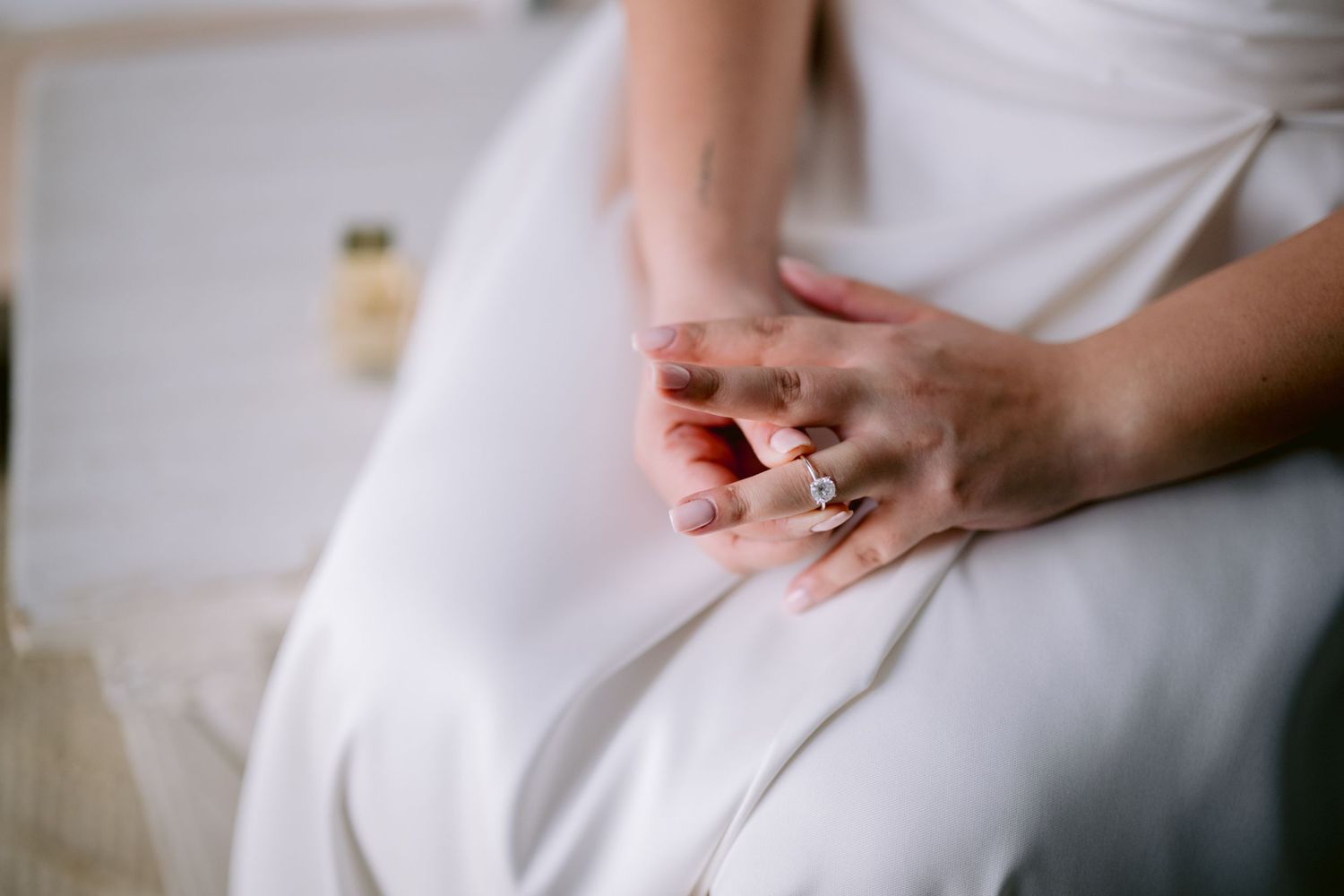 Close-up detail of hands resting on white wedding dress fabric.