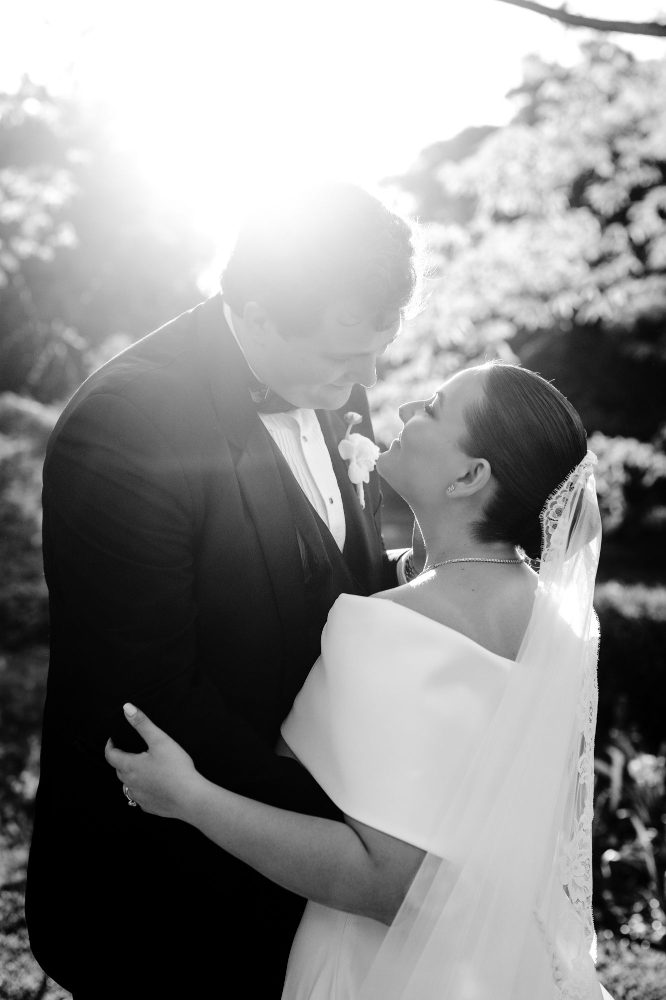 Romantic black and white portrait of a wedding couple sharing an intimate moment in a garden setting.