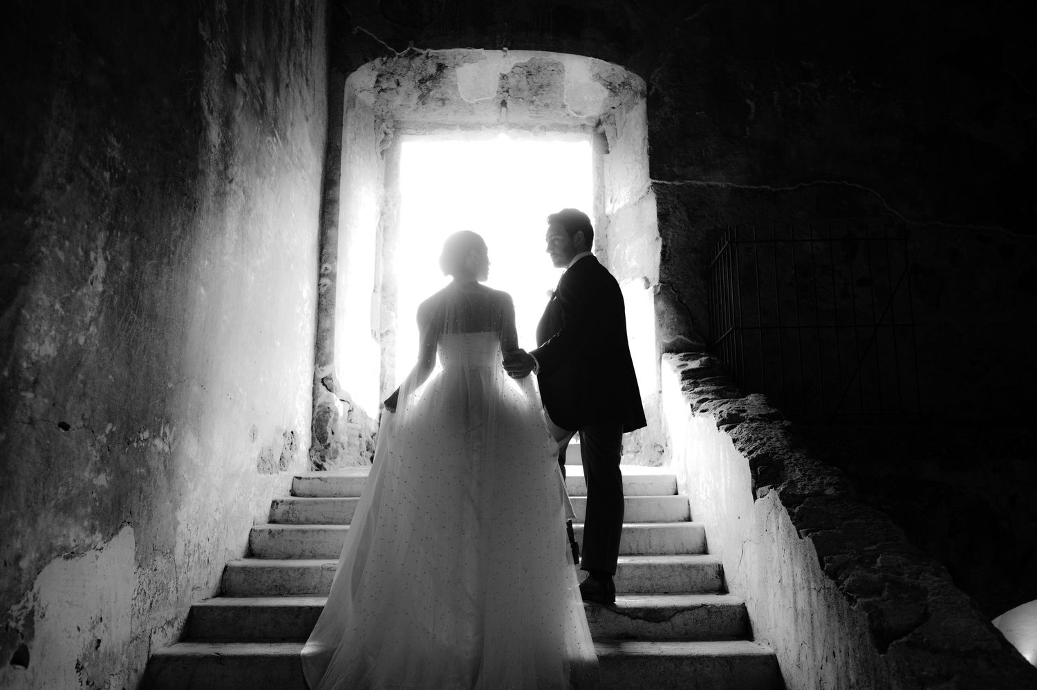Black and white silhouette of a wedding couple ascending stone stairs in dramatic lighting.