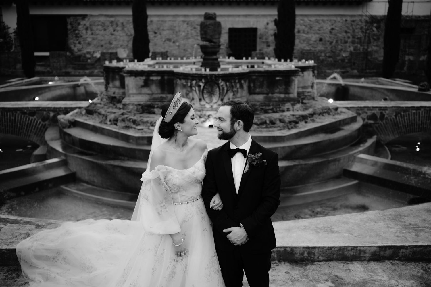 Black and white portrait of newlyweds by a tiered fountain at their historic venue wedding.
