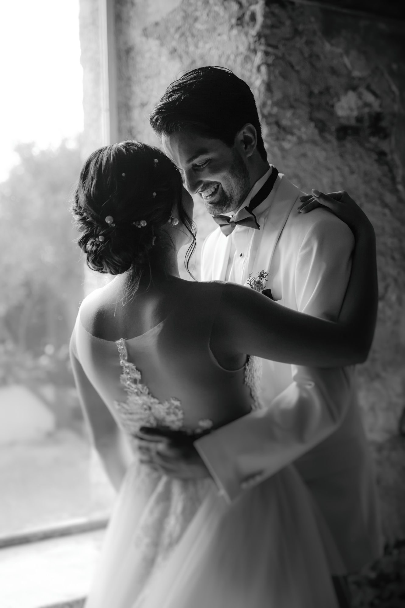 An intimate black and white portrait of newlyweds sharing a tender moment by a window.