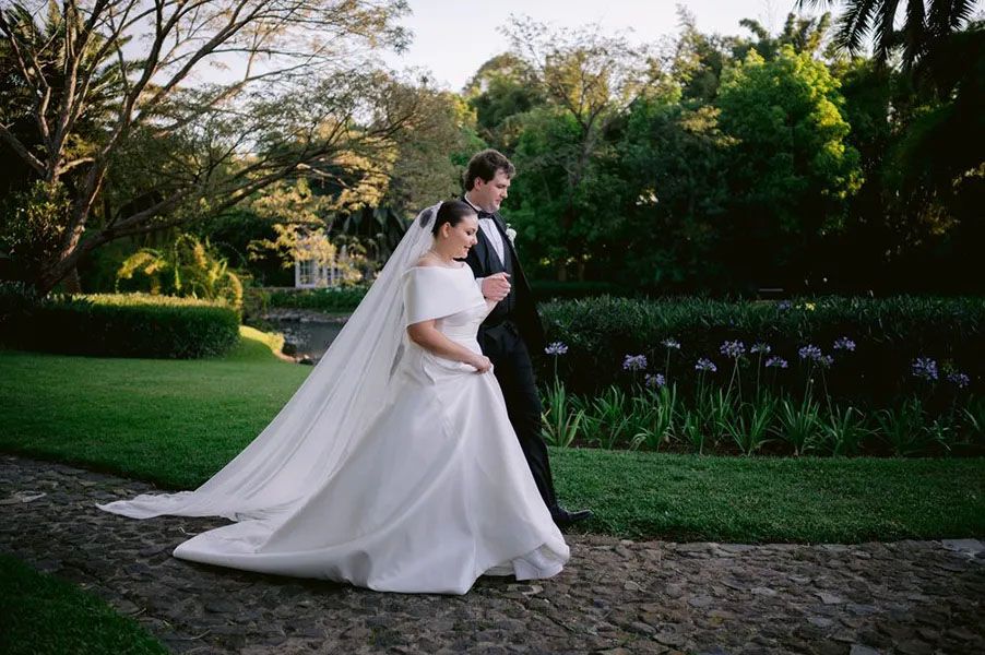 A romantic outdoor wedding scene with a couple dancing on a garden path surrounded by lush greenery.