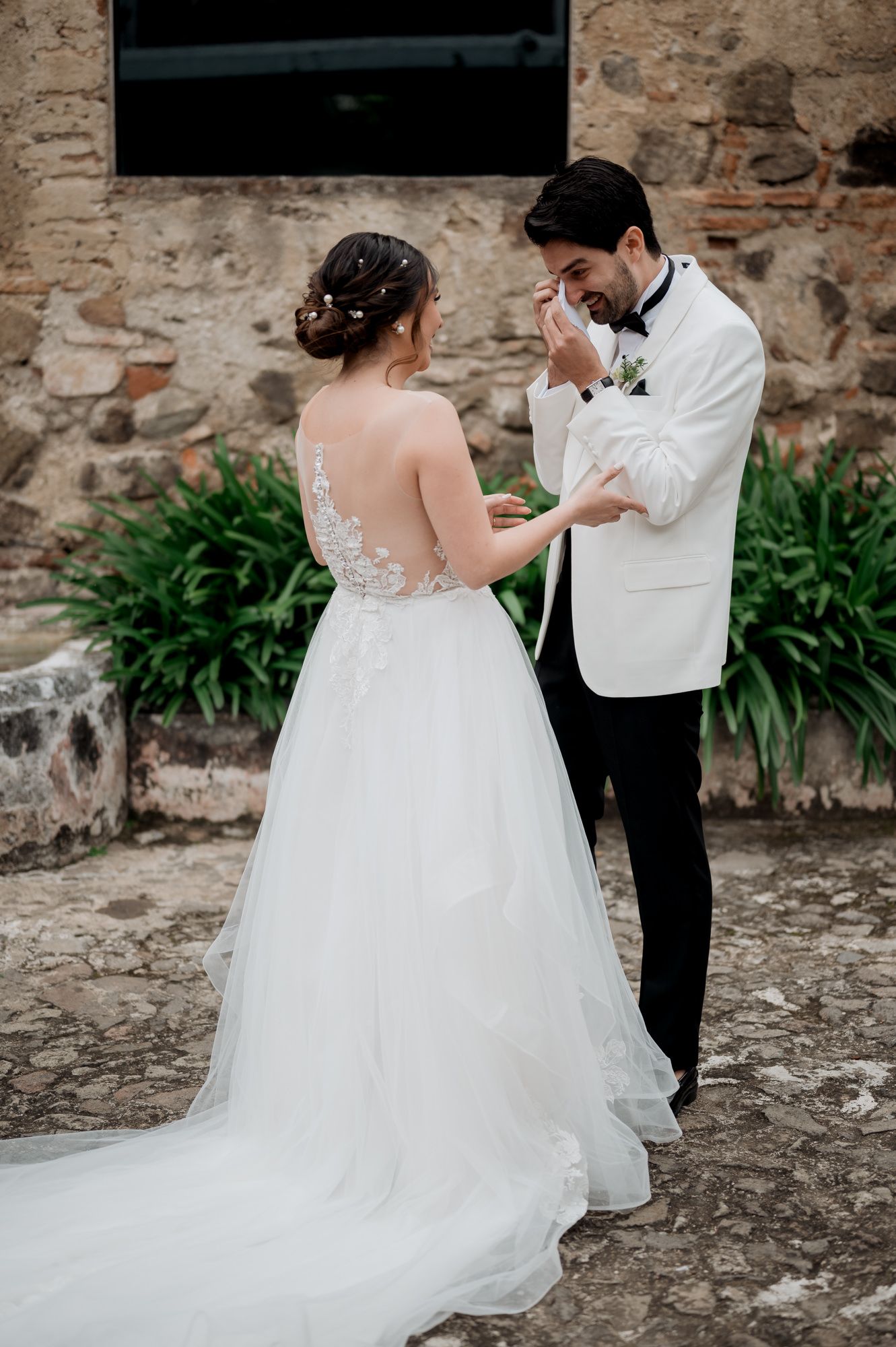 Emotional wedding reaction in white gown and tuxedo by stone wall.