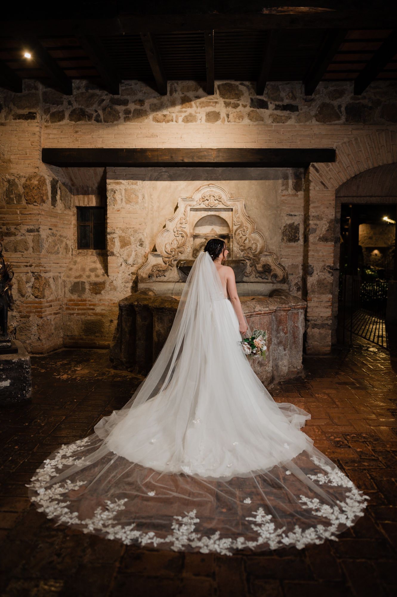 Long lace wedding train and veil photographed against historic stone wall.