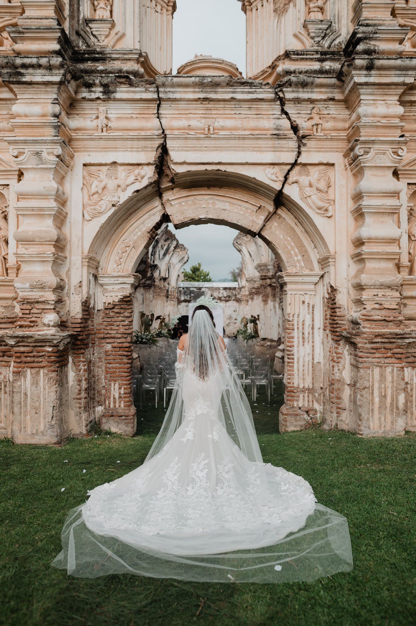 A stunning white wedding dress with long veil photographed against ancient ruins with ornate stone archways.