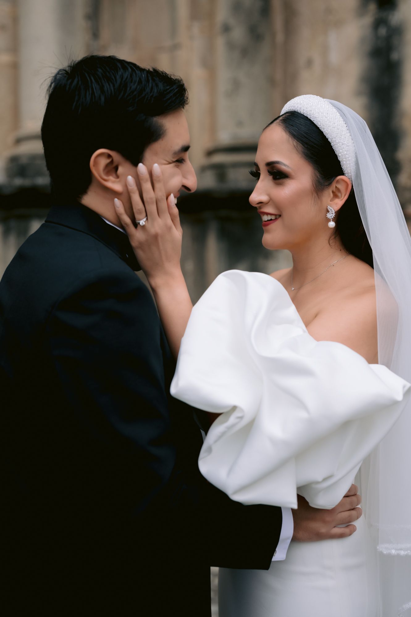 Intimate moment between couple in formal wedding attire against stone architecture.