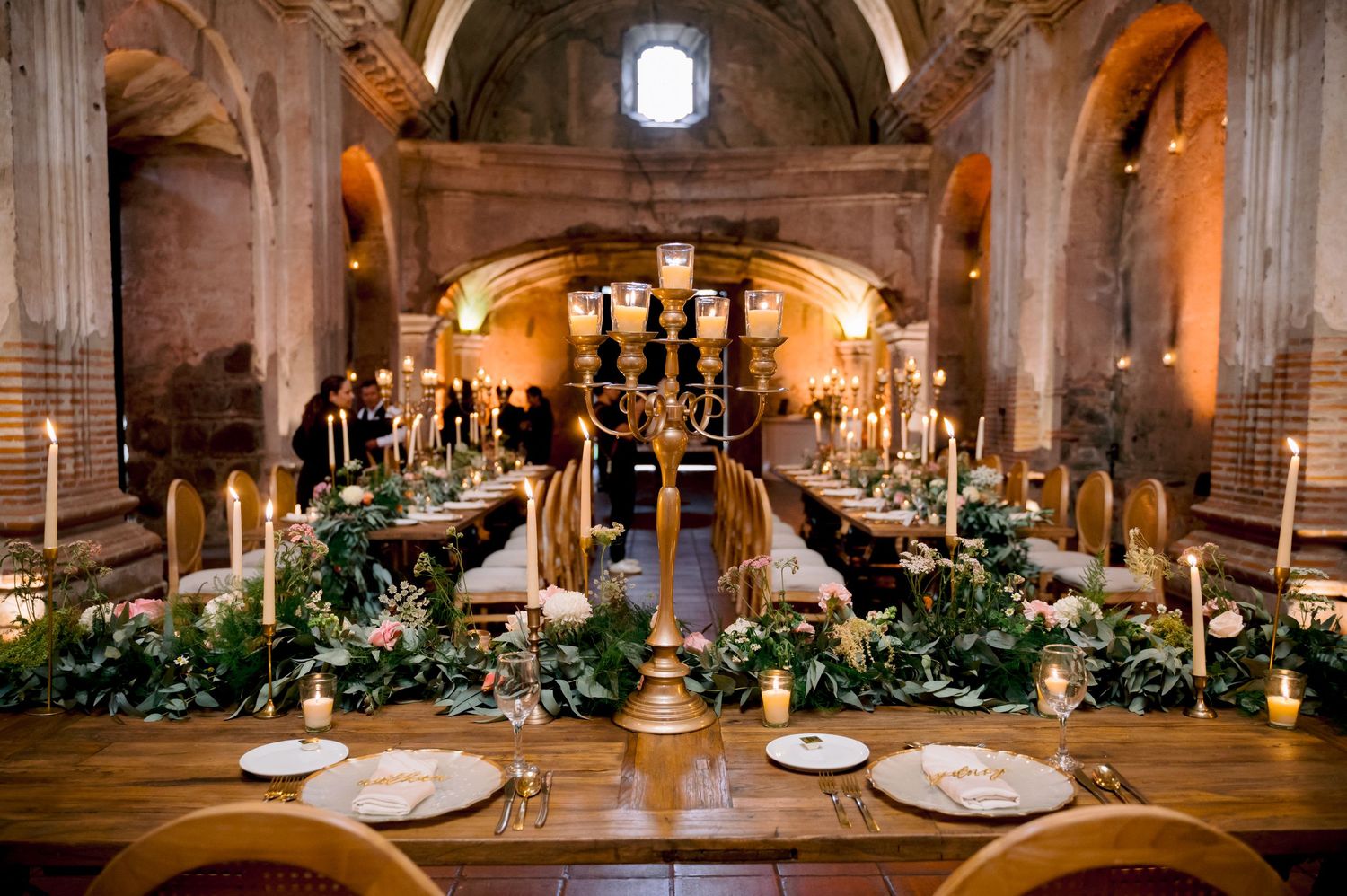 Romantic wedding reception setup in historic church with tall candelabras and lush table decorations.