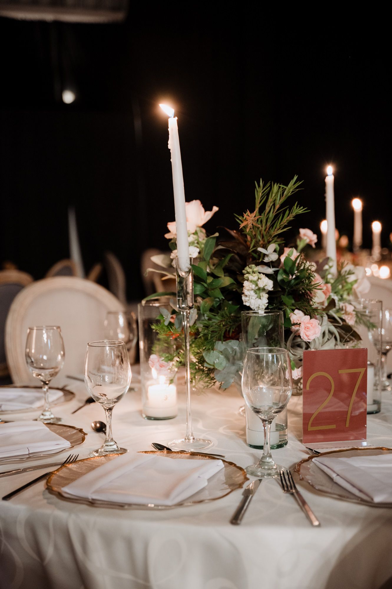 Elegant wedding table setting with tall white candles, delicate floral centerpieces and wine glasses.