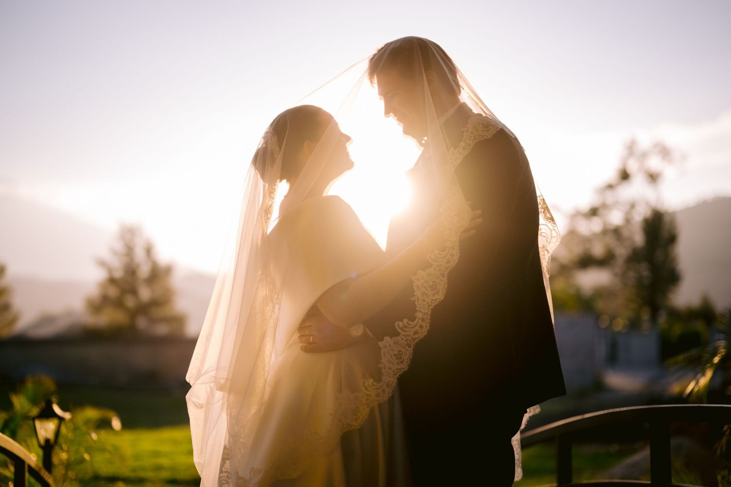 Backlit wedding portrait silhouetting couple against golden sunset mountain backdrop.