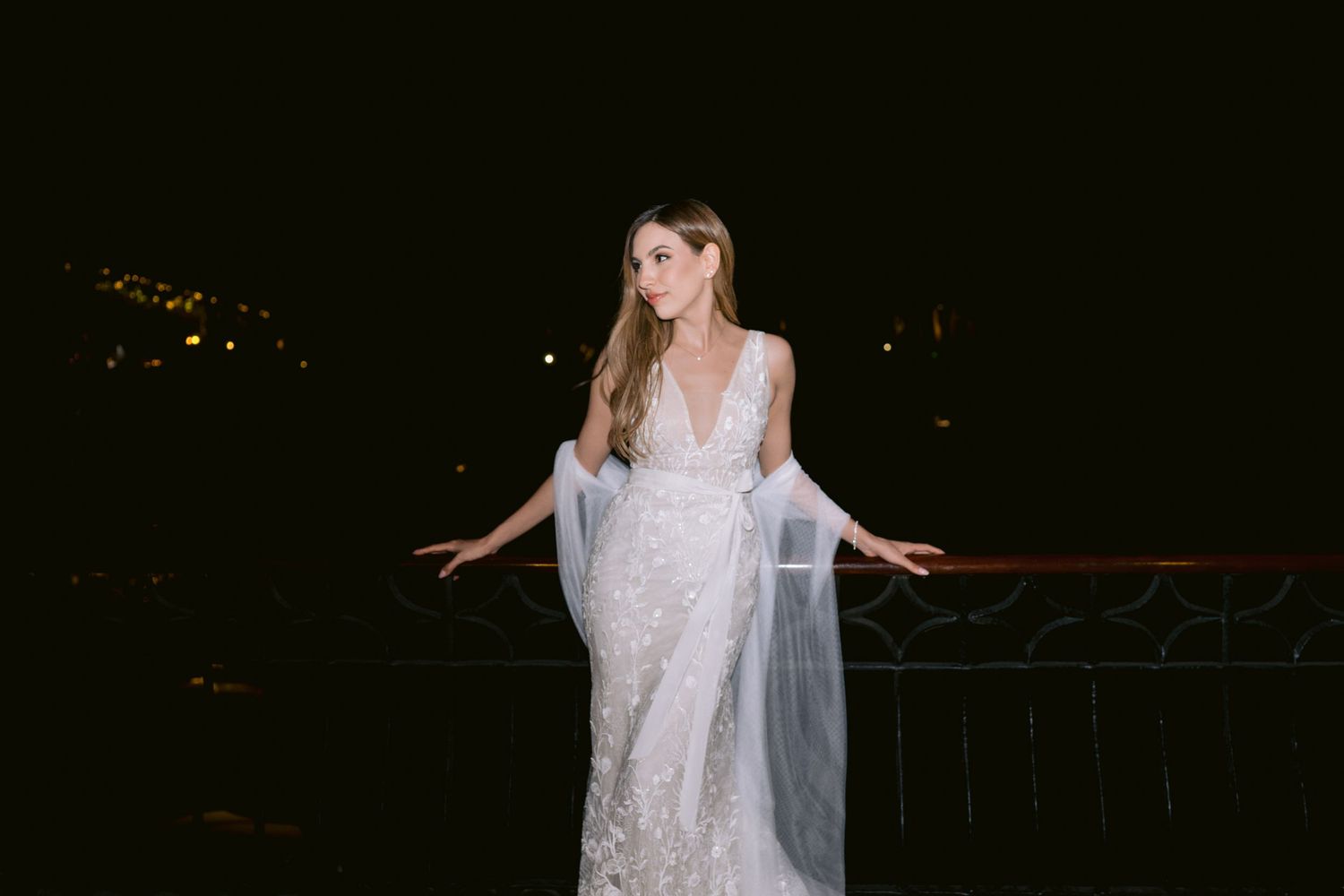 A person in a white lace dress performs a graceful dance pose against a dark background.