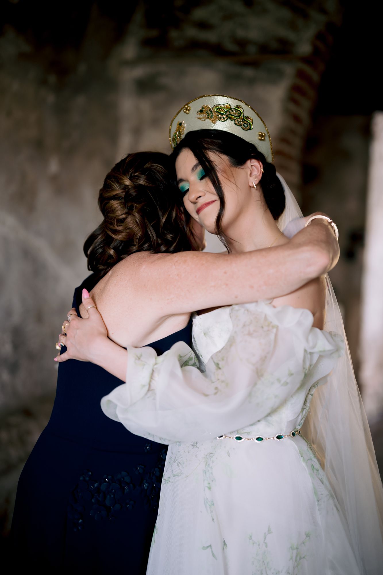 An emotional embrace between someone in navy blue and another in a white wedding dress with crown.