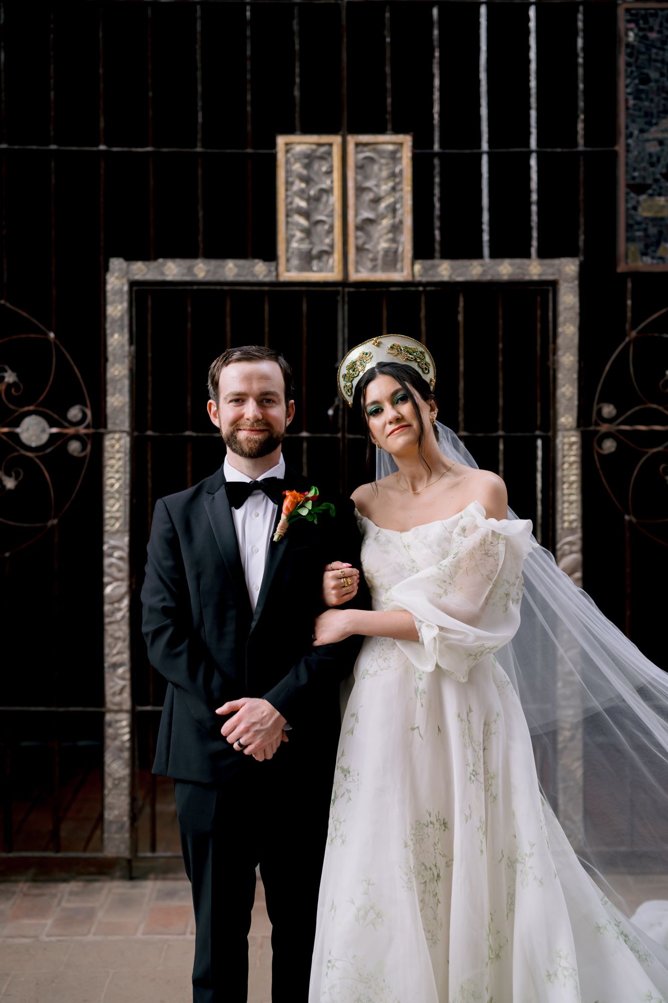 Wedding couple posing in formal attire against black iron gates at outdoor venue.