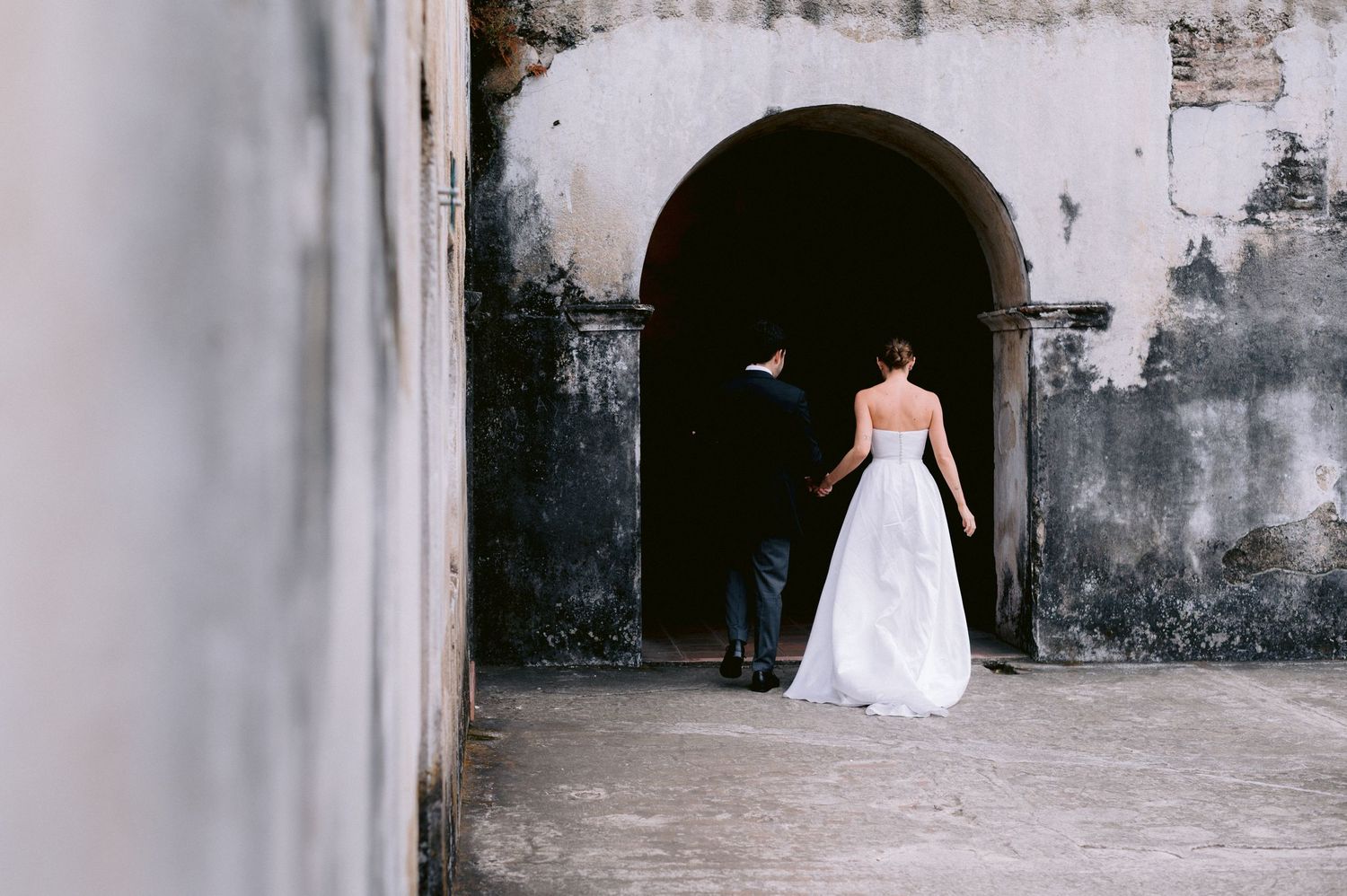 A bride in a white gown stands in an arched stone doorway.