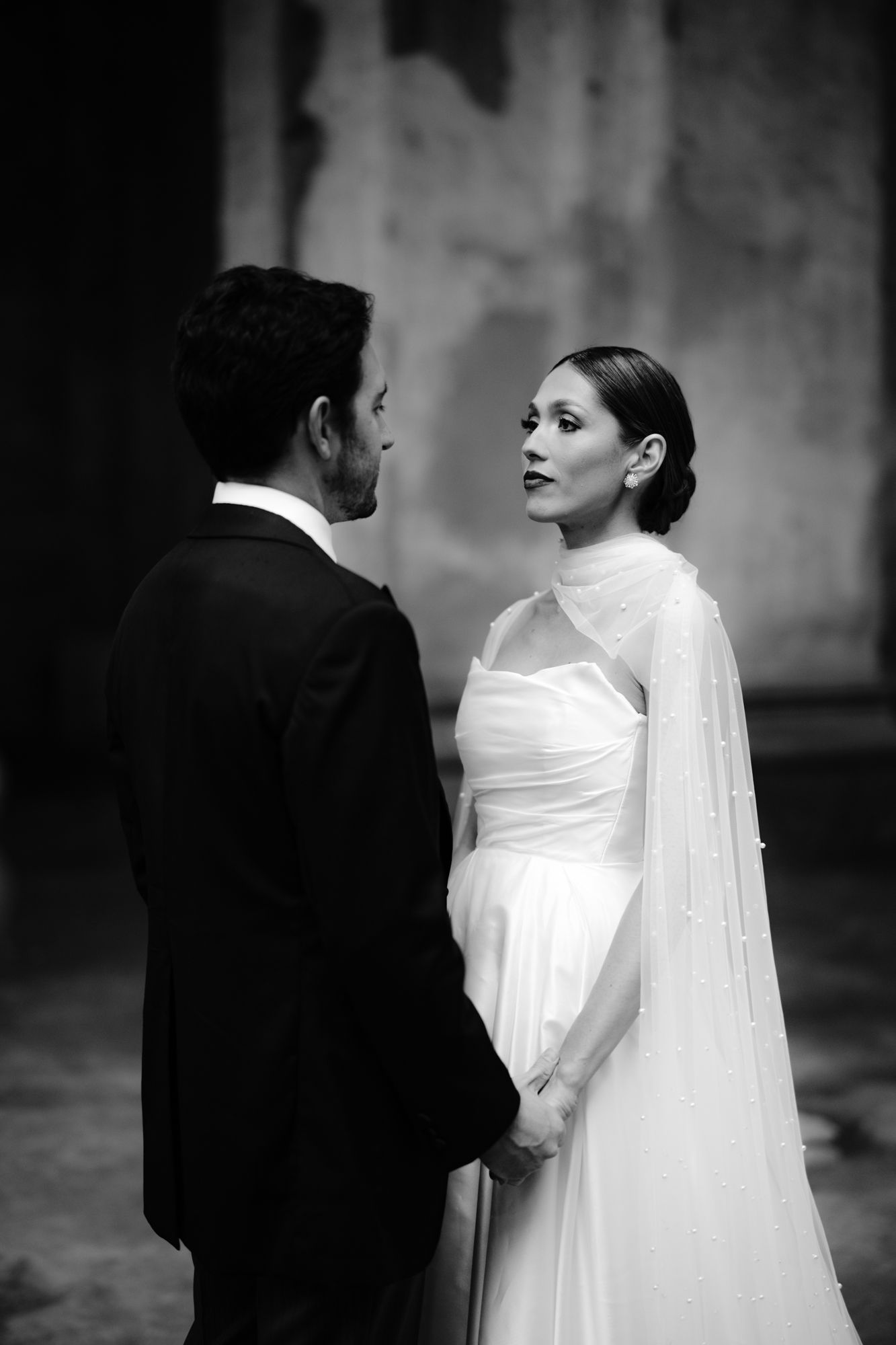 Black and white wedding portrait of couple in elegant attire standing face to face in romantic pose.