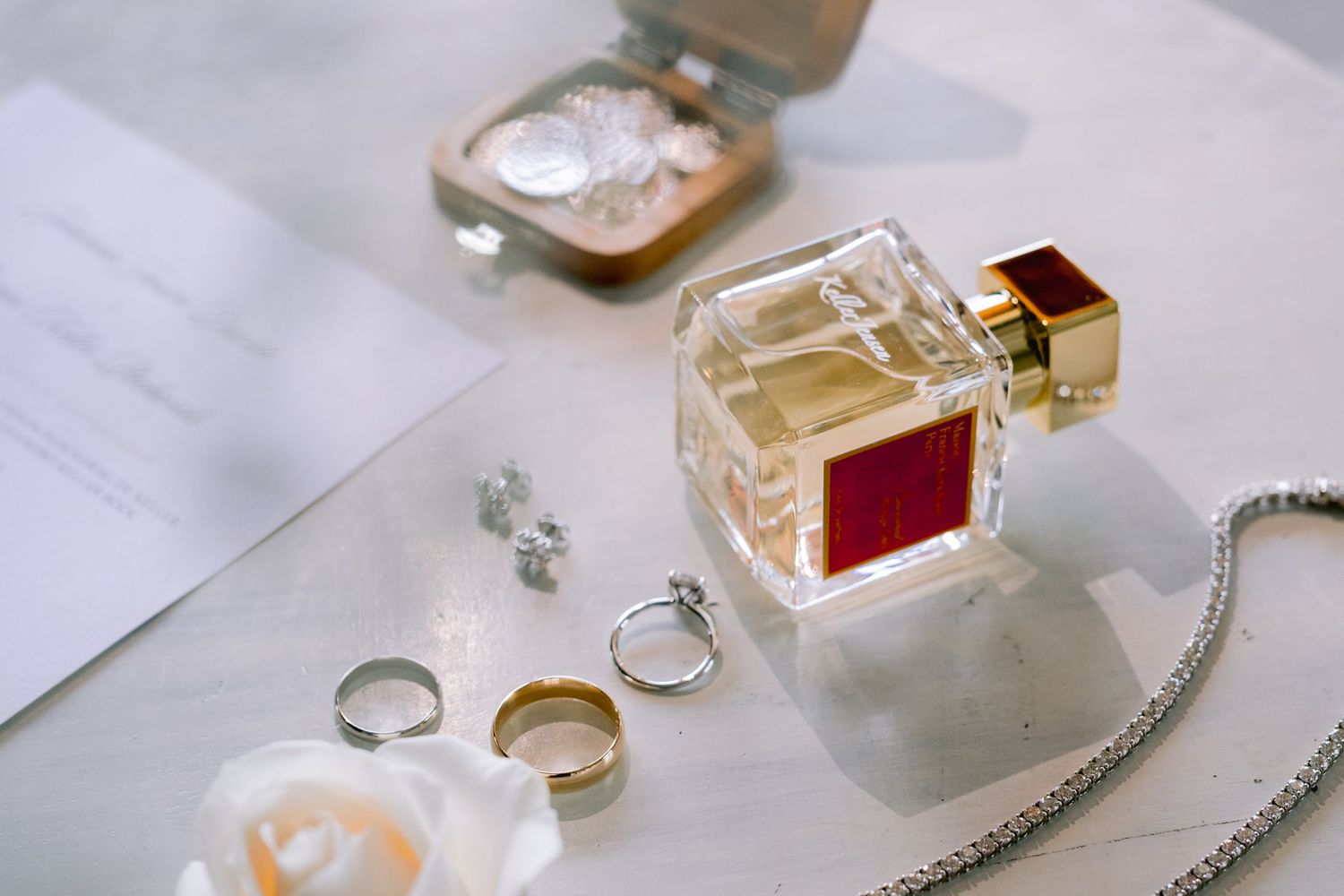 Wedding accessories including perfume bottle, rings and jewelry arranged on a light surface.