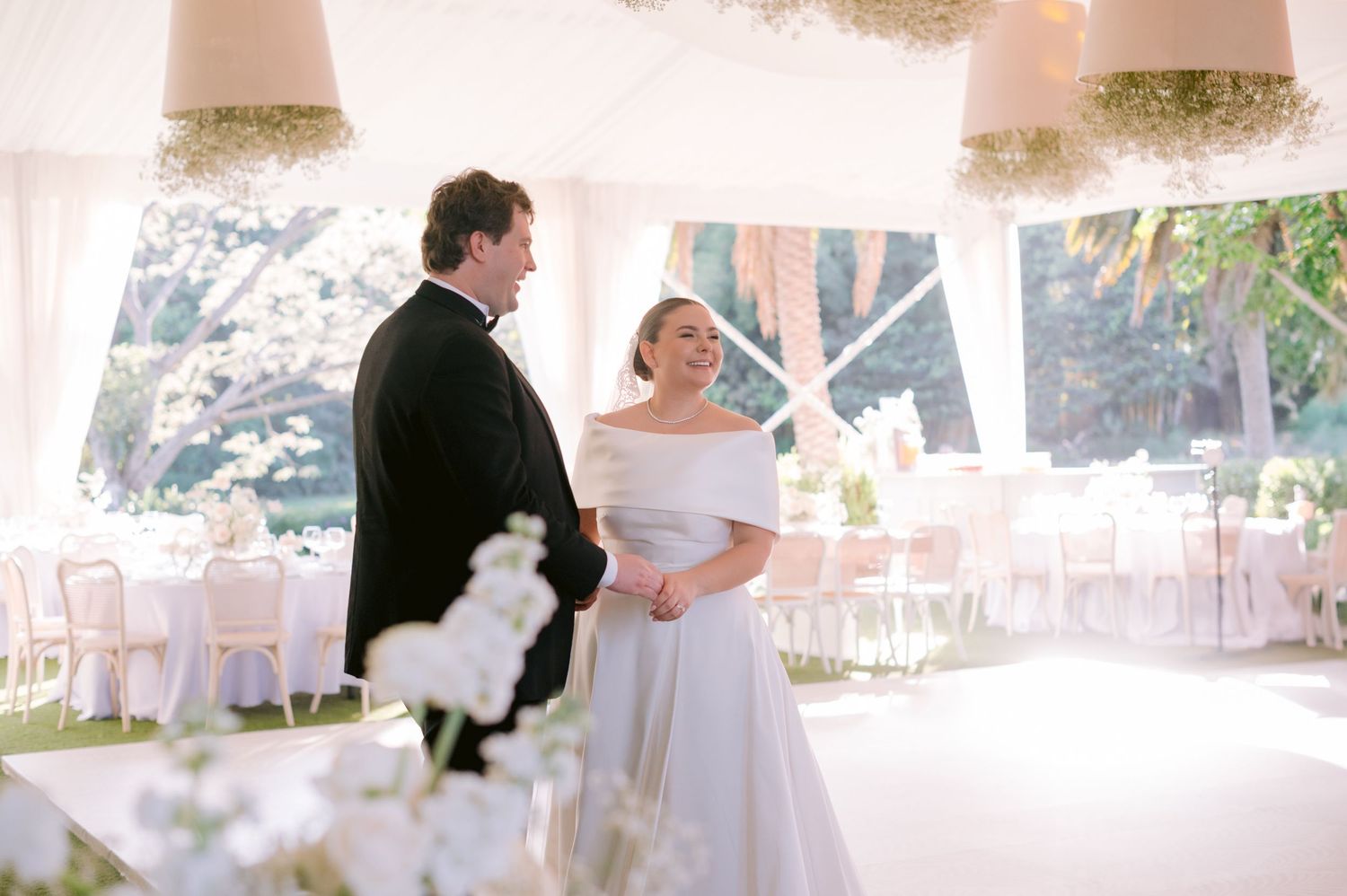 Elegant wedding reception setup with couple sharing a moment under white tent decor.