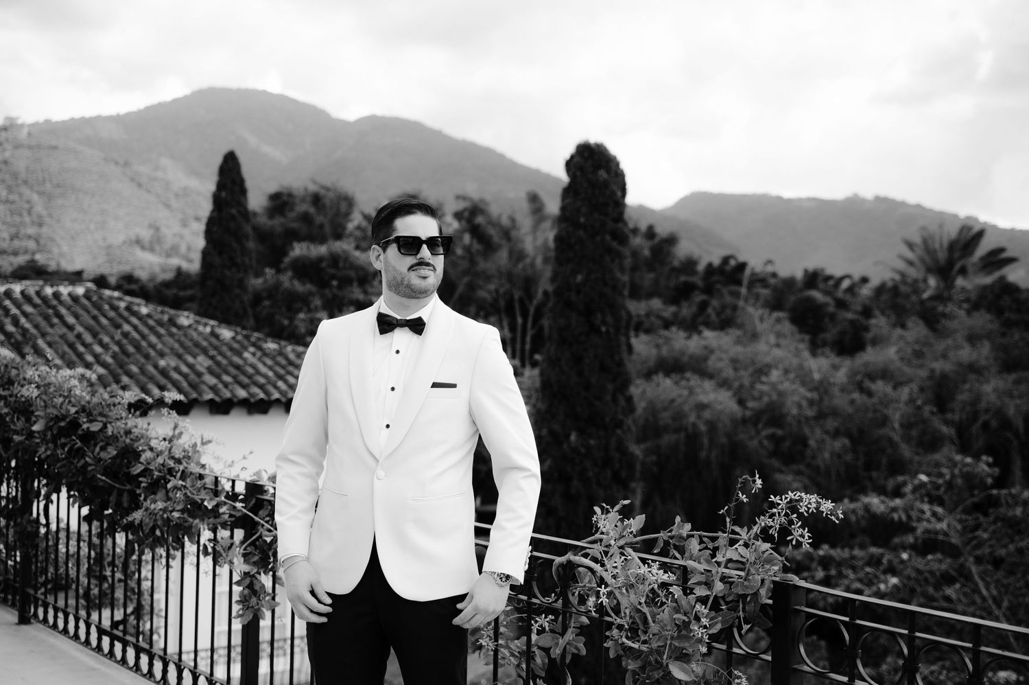 A black and white photo montage of a person in formal attire against scenic mountain and architectural backdrops.