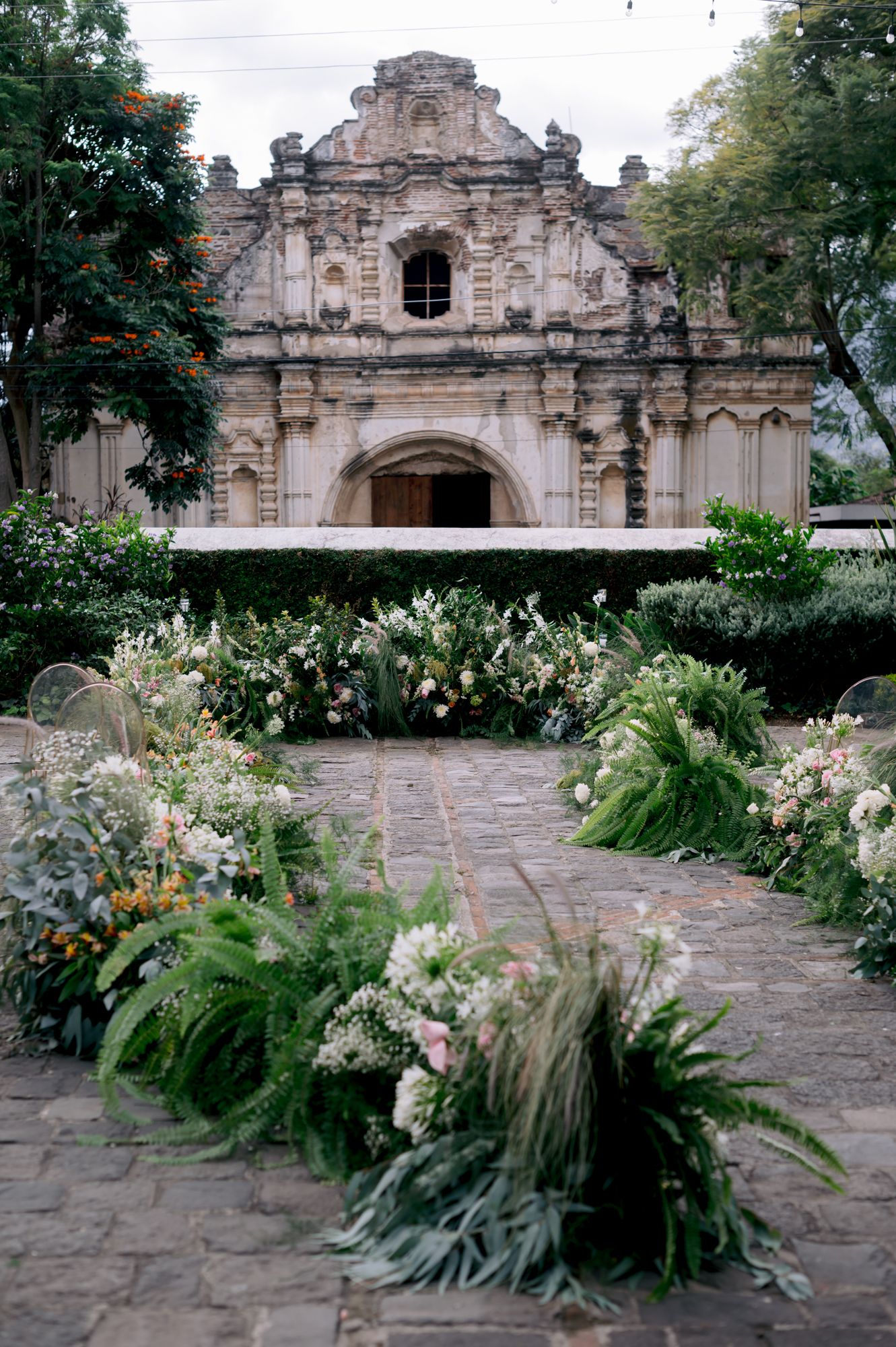Historic stone church facade with ornate baroque details surrounded by lush floral arrangements.