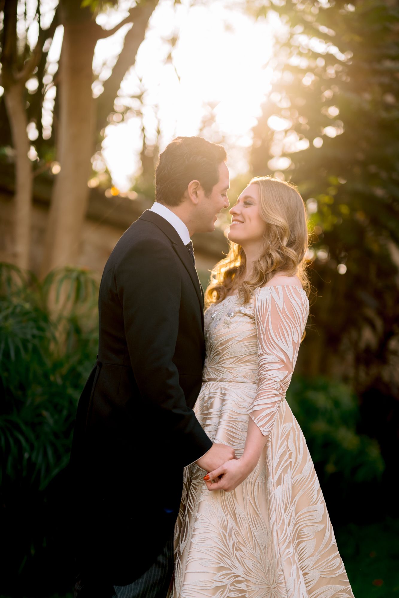 A romantic sunset portrait of a couple in wedding attire surrounded by golden light and greenery.