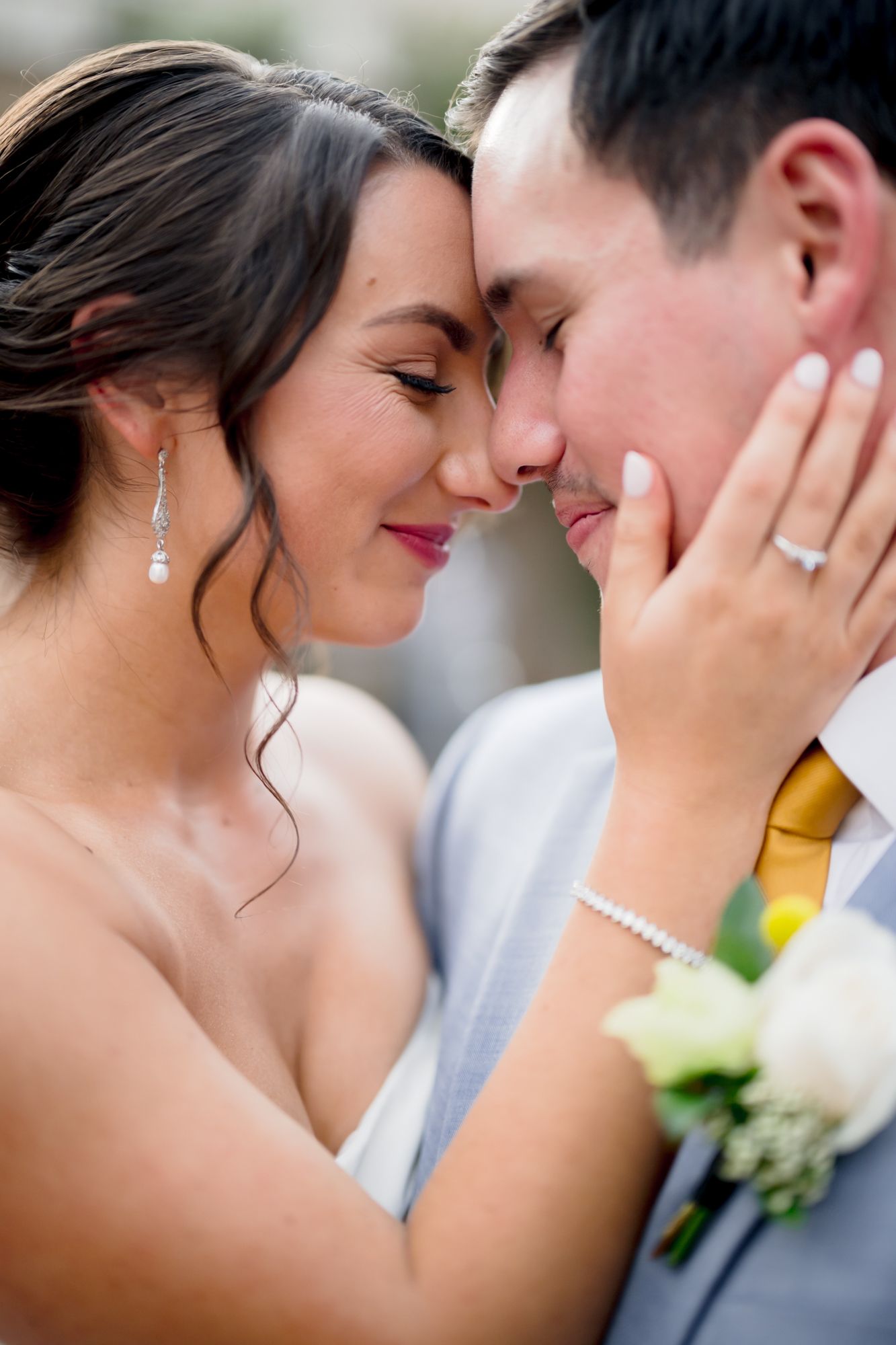 A romantic close-up of newlyweds sharing an intimate moment, with the bride wearing dangling earrings and a pearl bracelet.