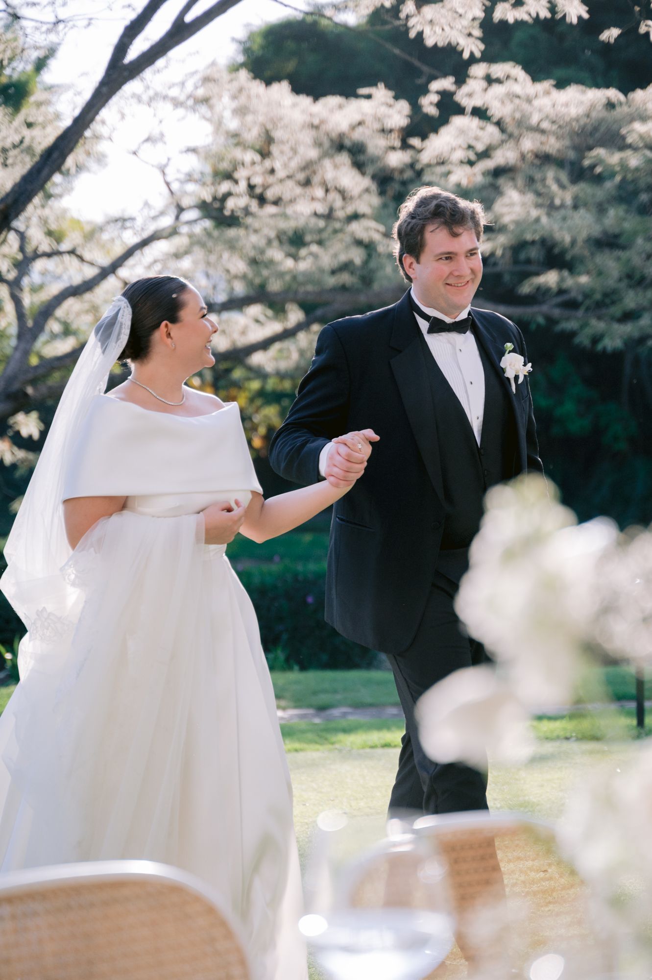 Wedding couple holding hands under blooming cherry blossom trees.