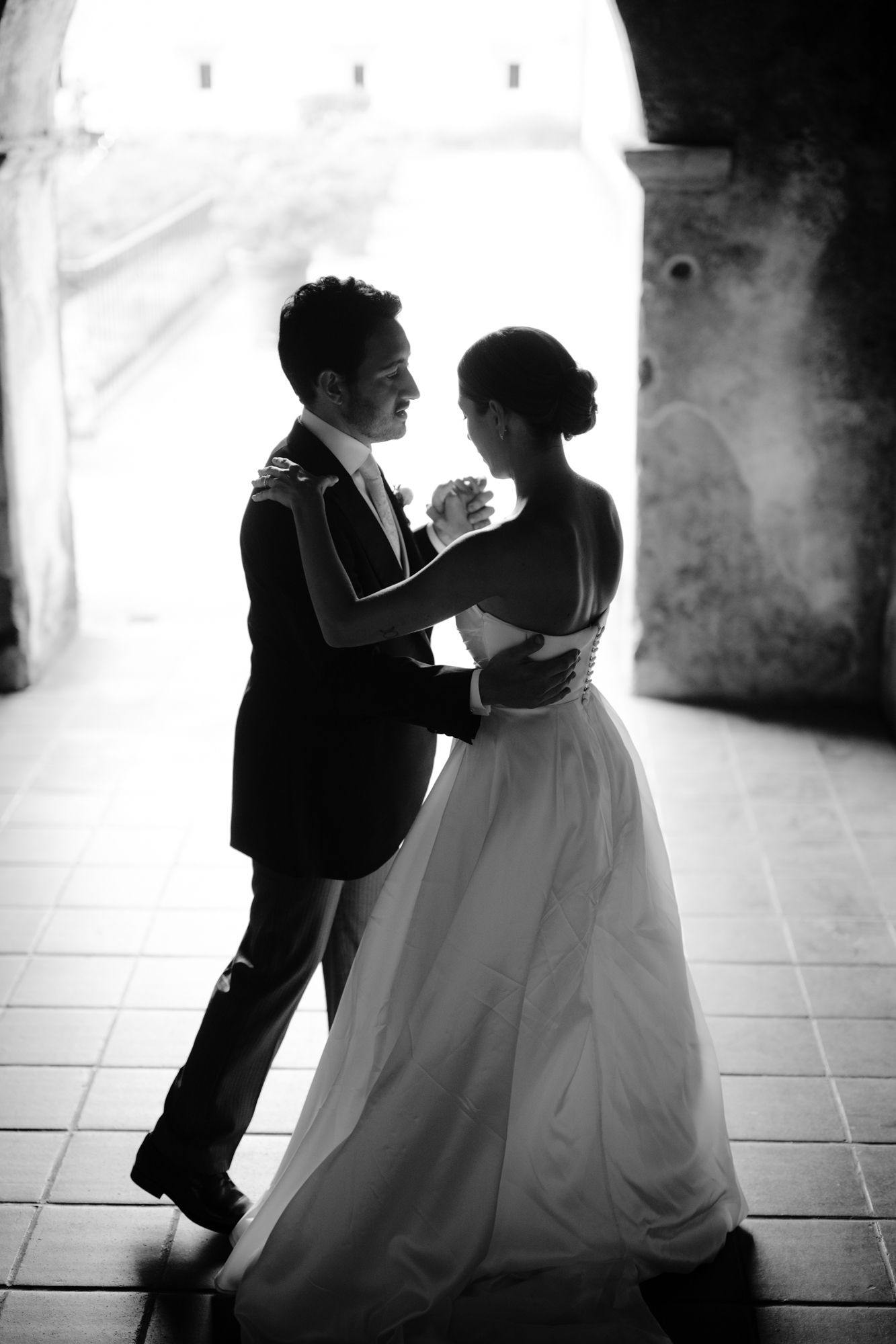 Black and white photo of a couple dancing in formal attire under an arched doorway.