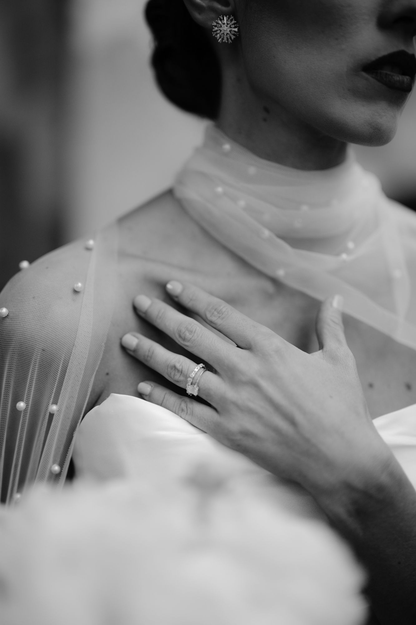 Close-up black and white photo of a pearl-studded wedding veil and engagement ring.