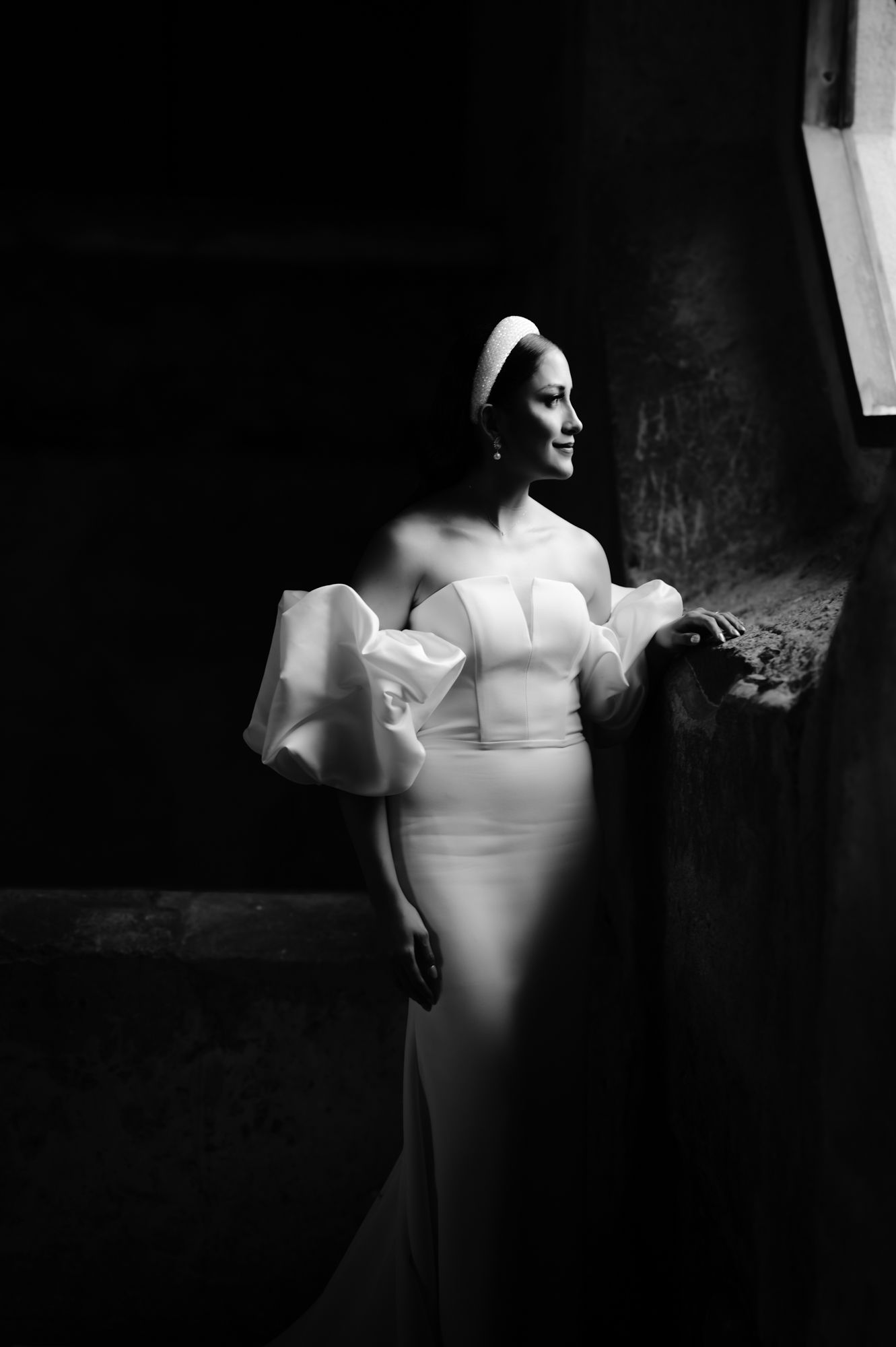 Elegant bride in fitted white gown with statement sleeves poses against textured wall.