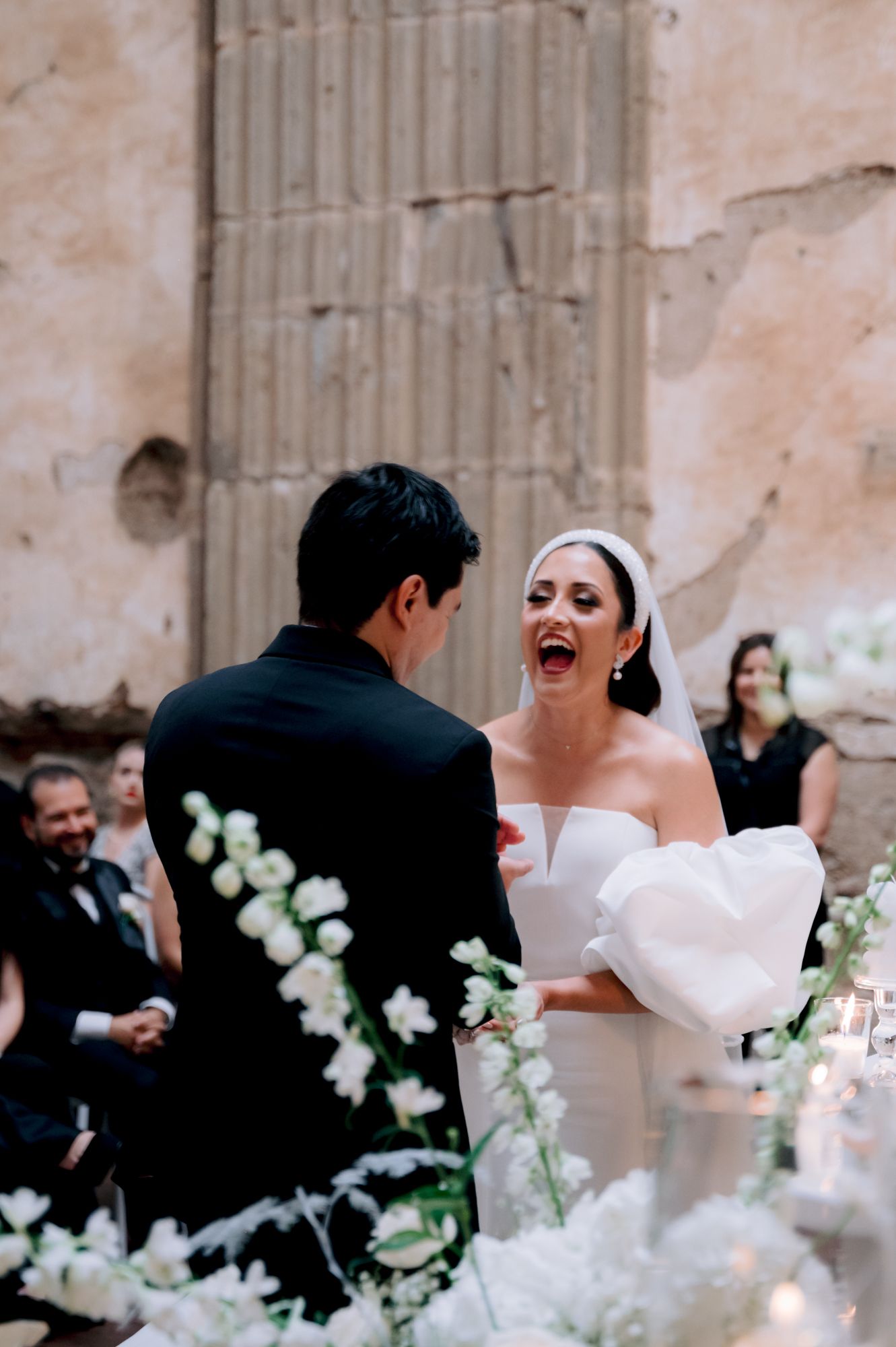 Joyful wedding ceremony moment with white floral decorations against historic stone wall.