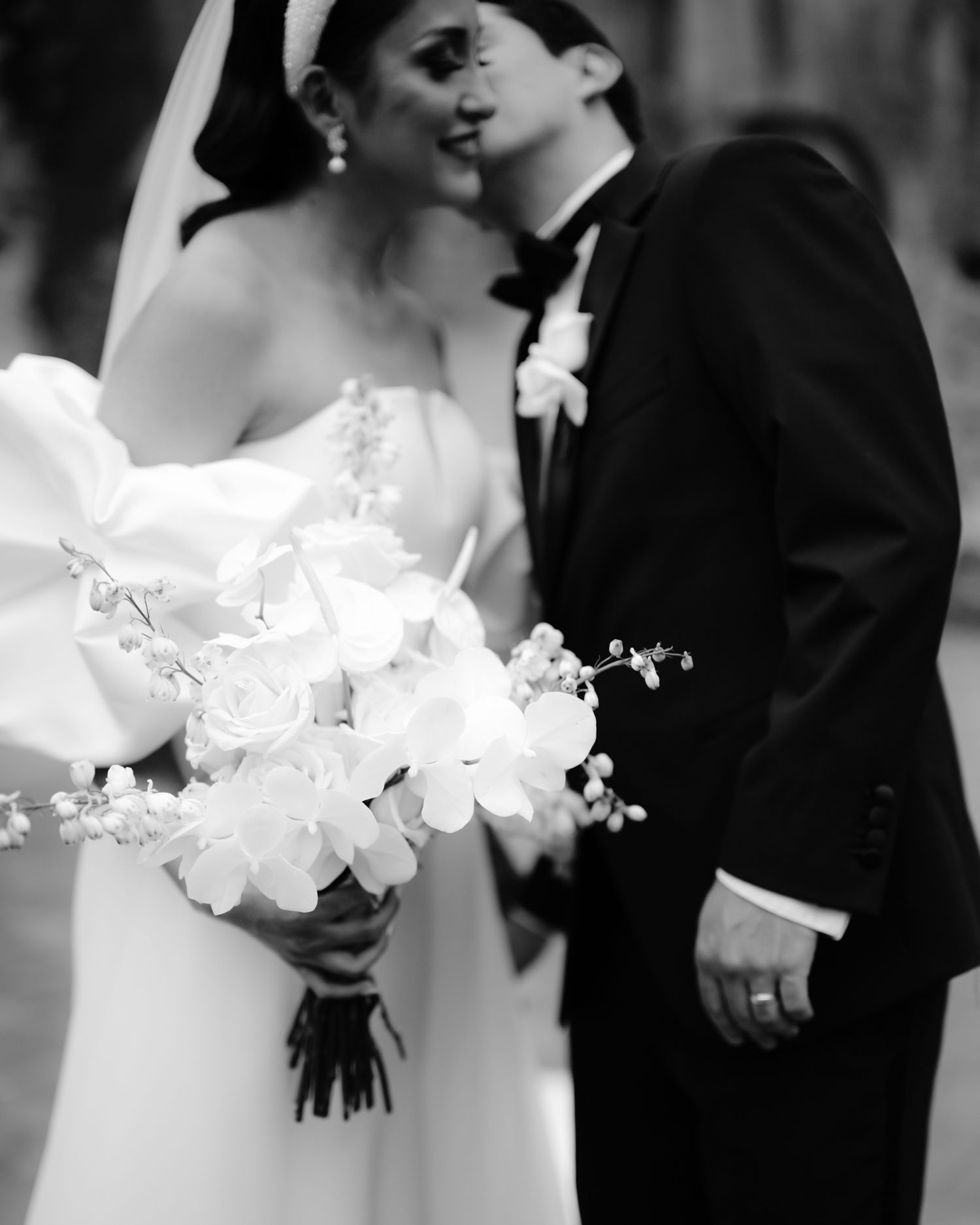 Intimate black and white photo of newlyweds sharing a tender moment with a white floral bouquet.
