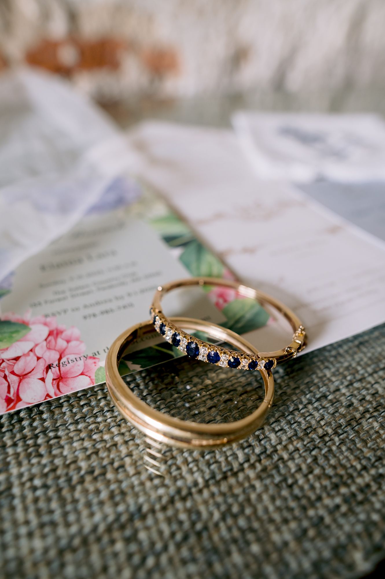 Two wedding rings displayed on textured fabric next to a floral invitation.