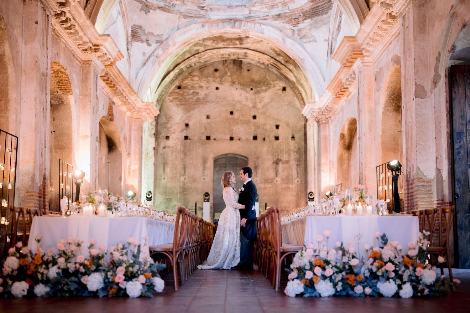 A wedding reception setup in a historic church with long tables and pink floral decorations.