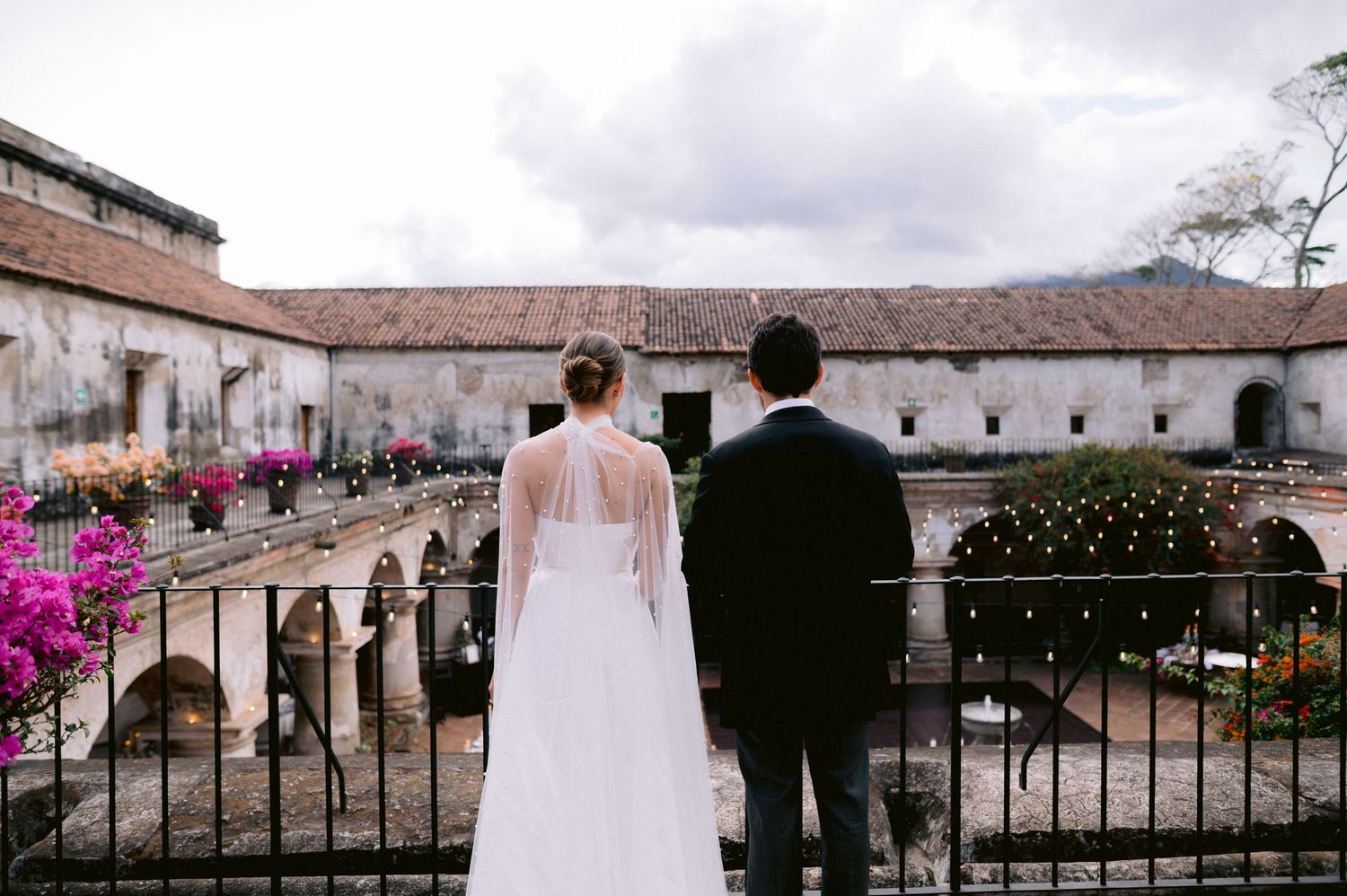 A couple overlooking a Spanish colonial courtyard with pink bougainvillea flowers.