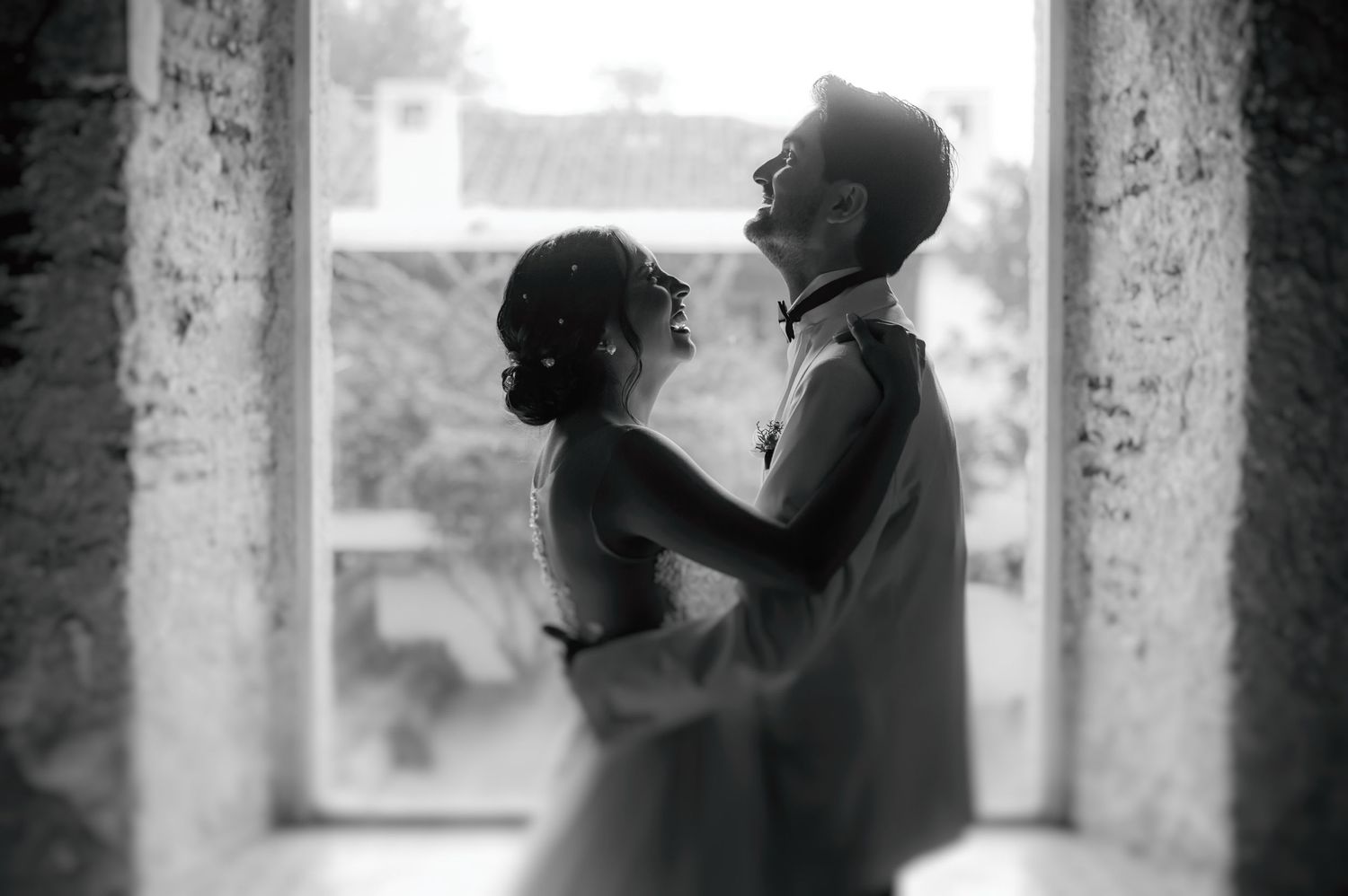 A romantic black and white photograph of a couple embracing near a window in an old building.