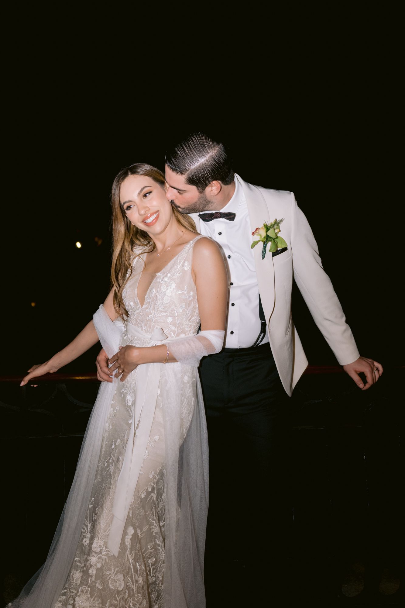 Couple dancing together at a wedding reception in formal attire against a dark background.