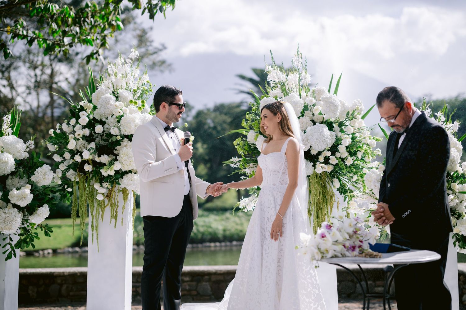 Wedding ceremony with white floral decorations and columns in an elegant outdoor garden setting.