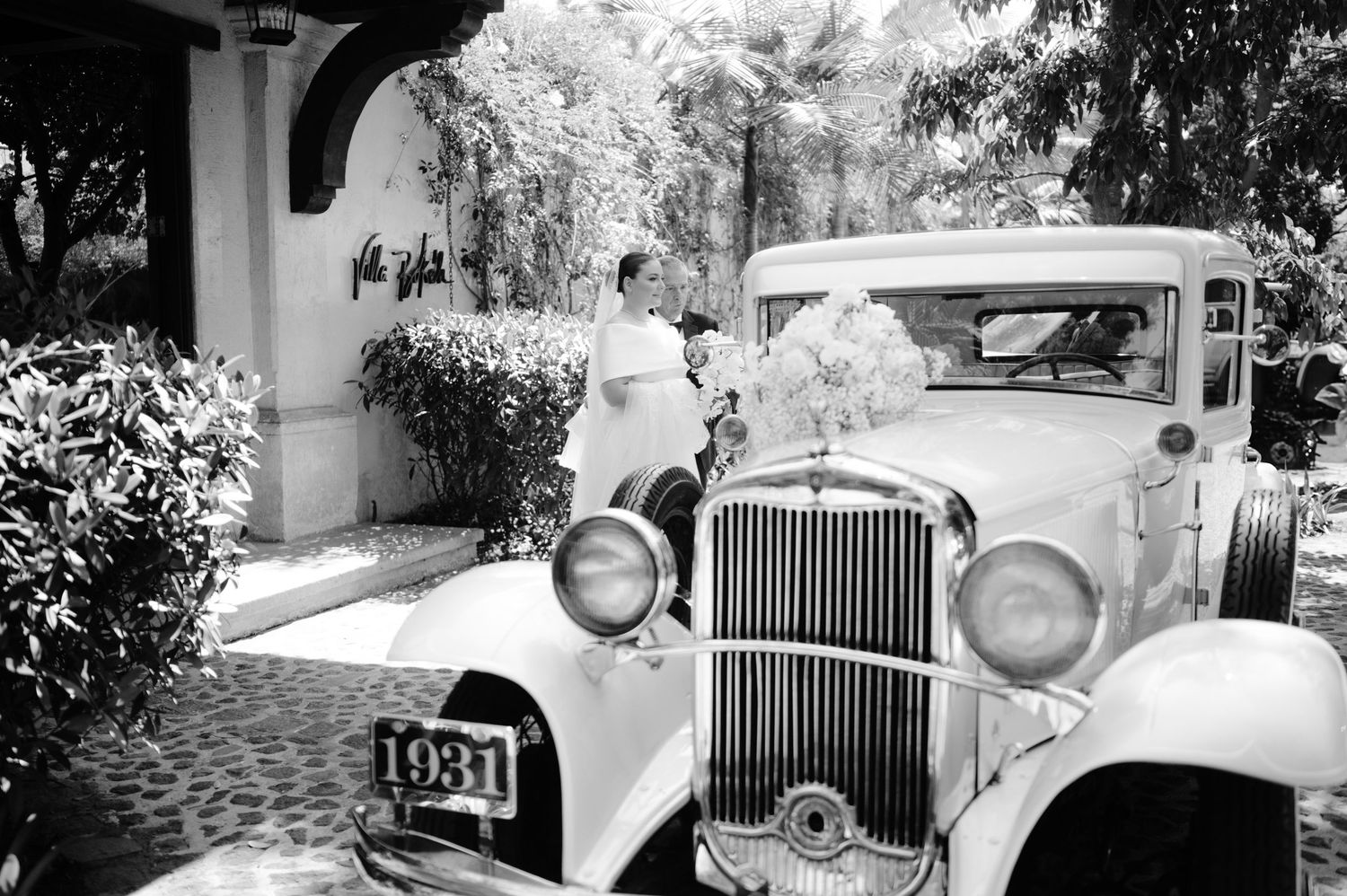 A vintage white classic car parked near an arched colonnade for a wedding.