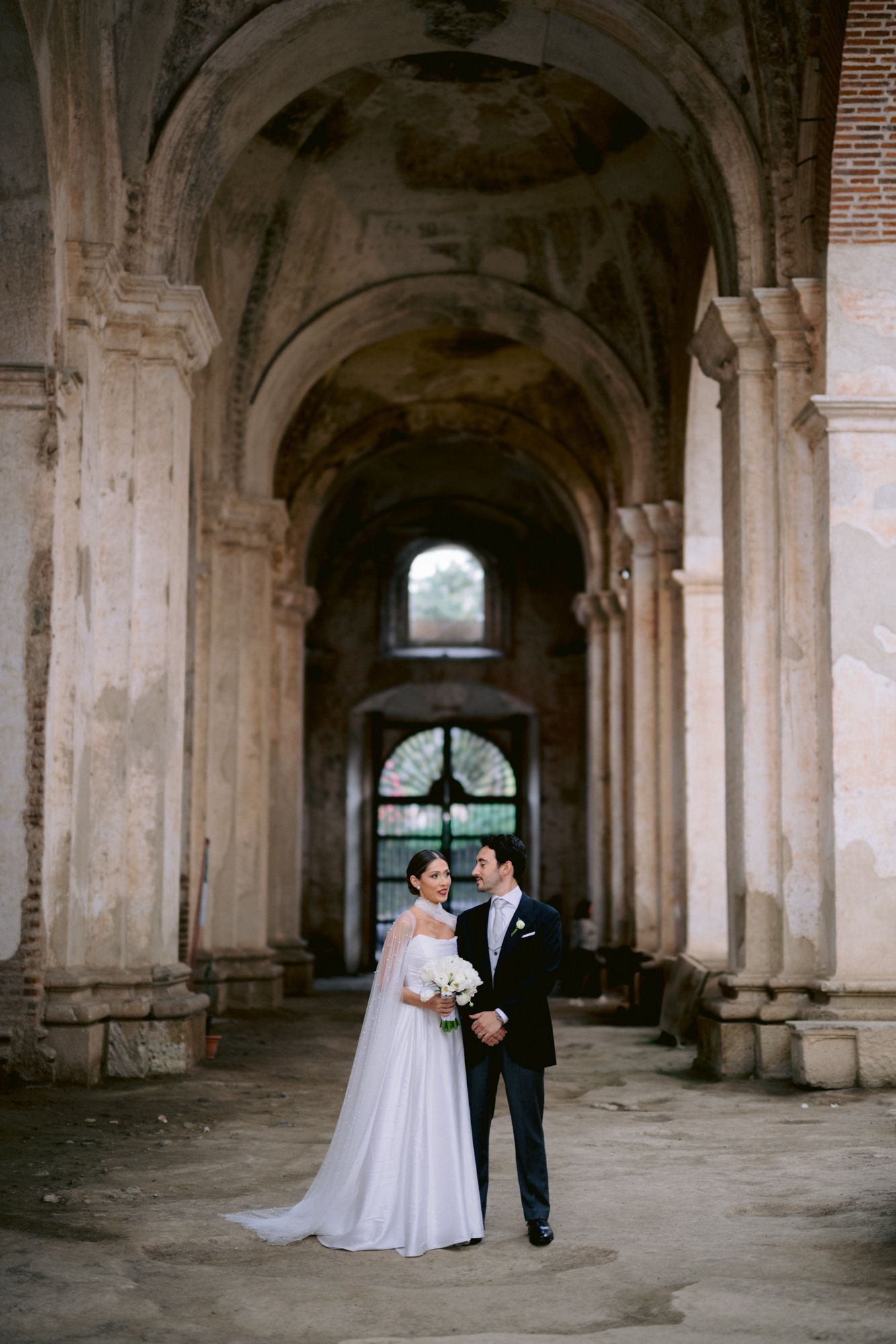 Newlyweds pose together under magnificent stone archways in historic setting.