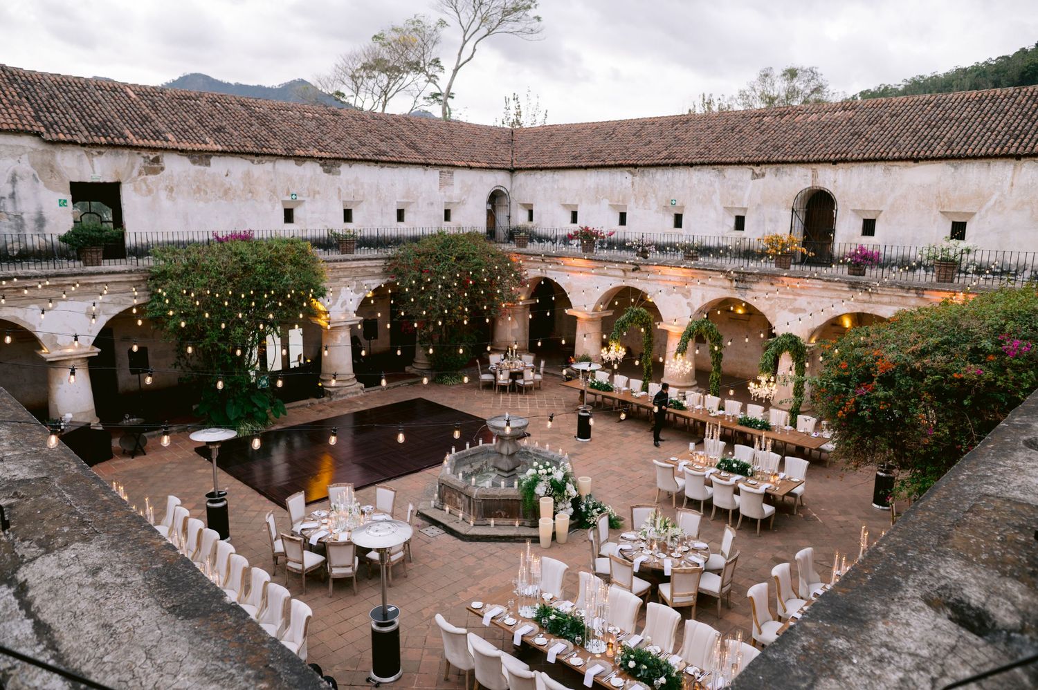 Elegant outdoor wedding reception setup in a Spanish colonial courtyard with fountain and white table settings.