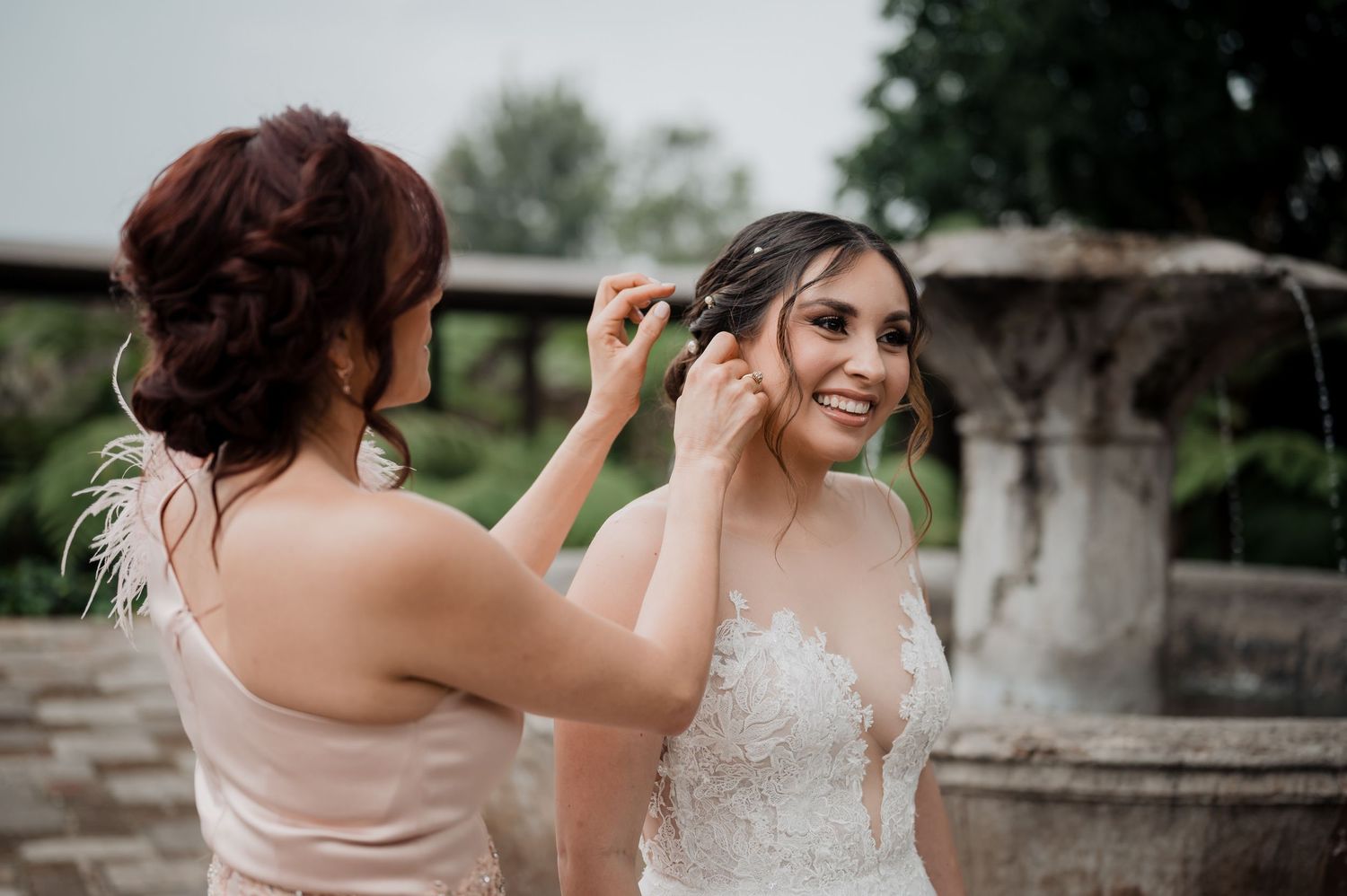 Final wedding preparation moments shared between two people near a stone fountain.
