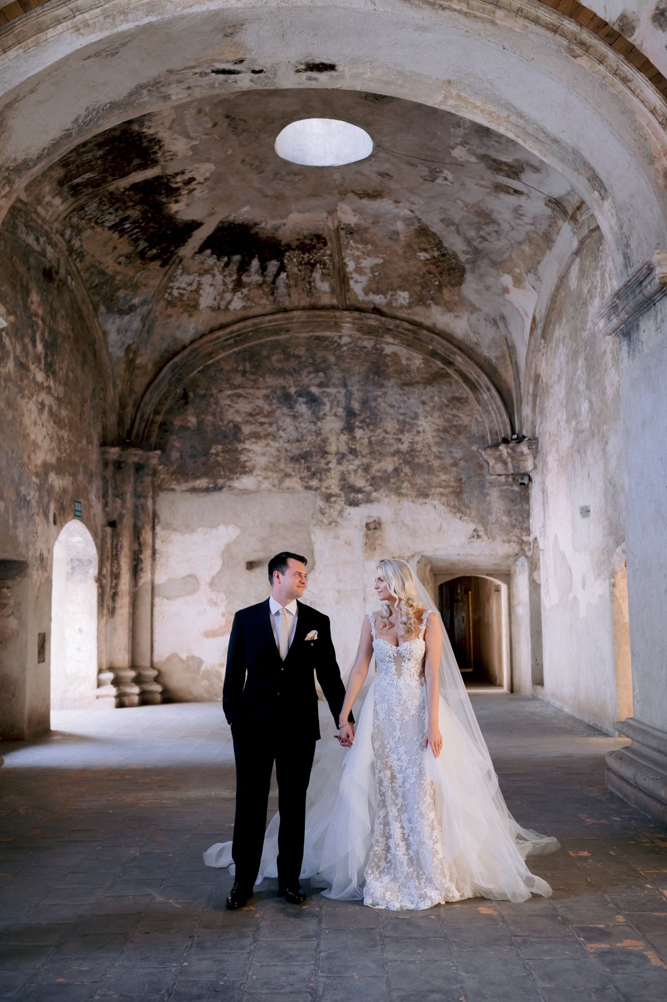Wedding couple stands beneath domed ceiling in historic stone architecture.