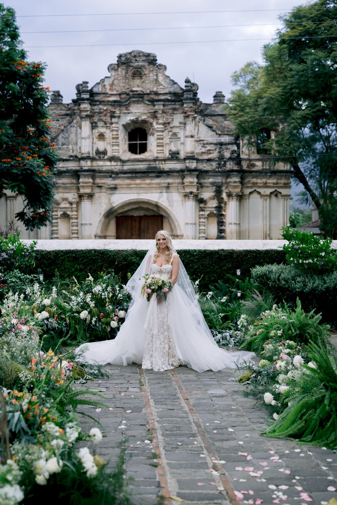 A wedding ceremony venue with ornate colonial architecture and lush garden landscaping along a stone pathway.