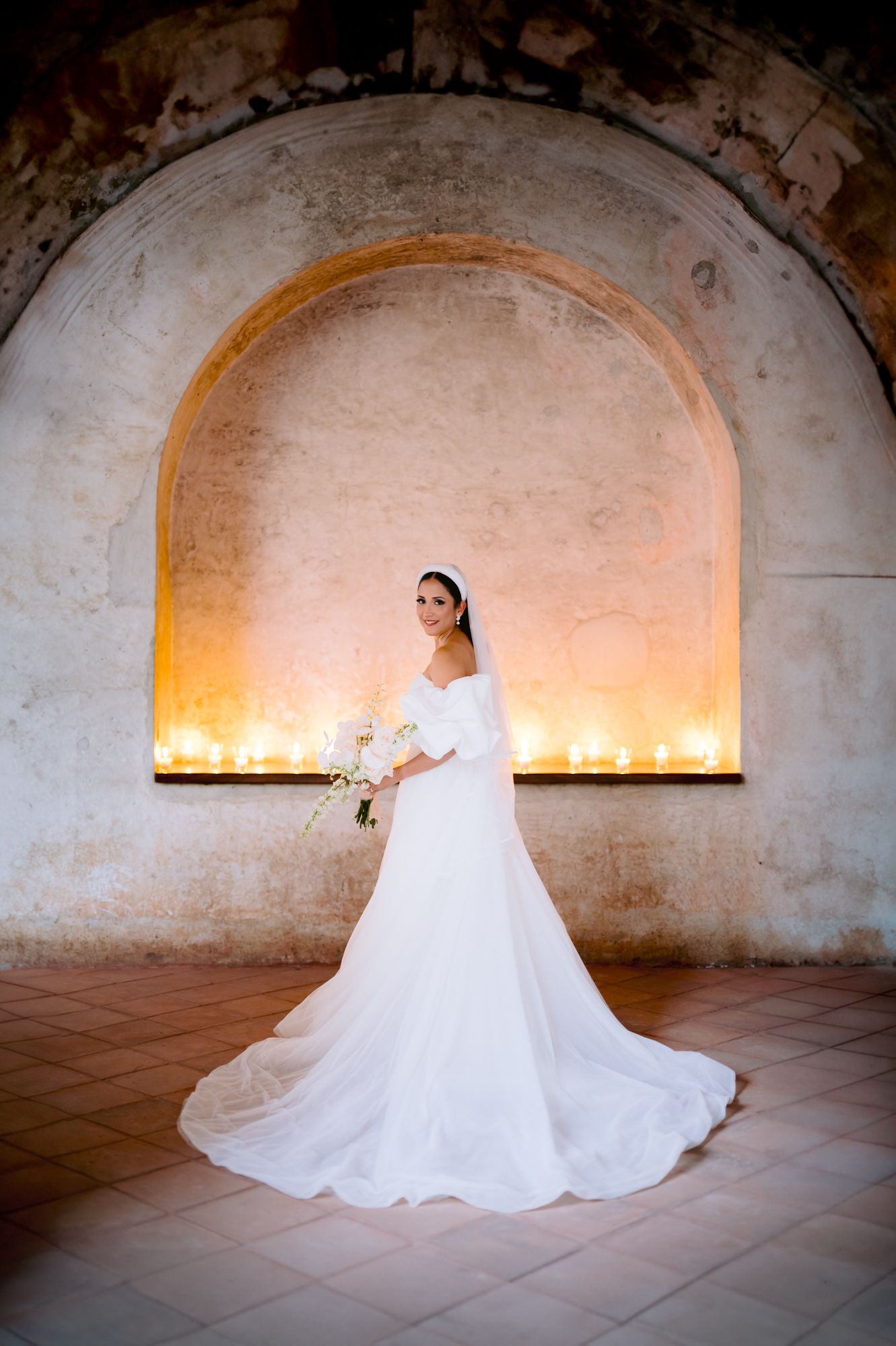 Bridal portrait in illuminated stone archway with candlelight and flowing train of white wedding gown.