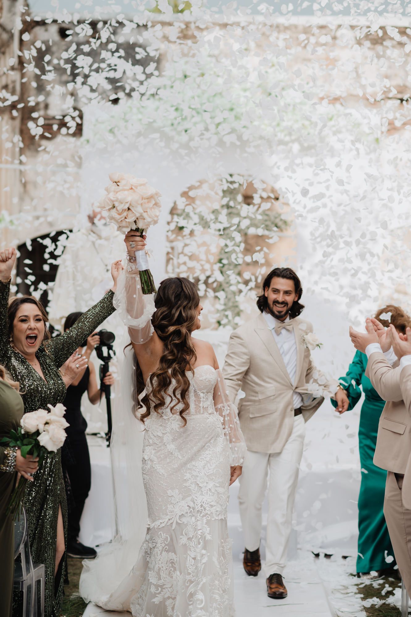 Wedding celebration with guests dancing and confetti falling in an elegant white venue.