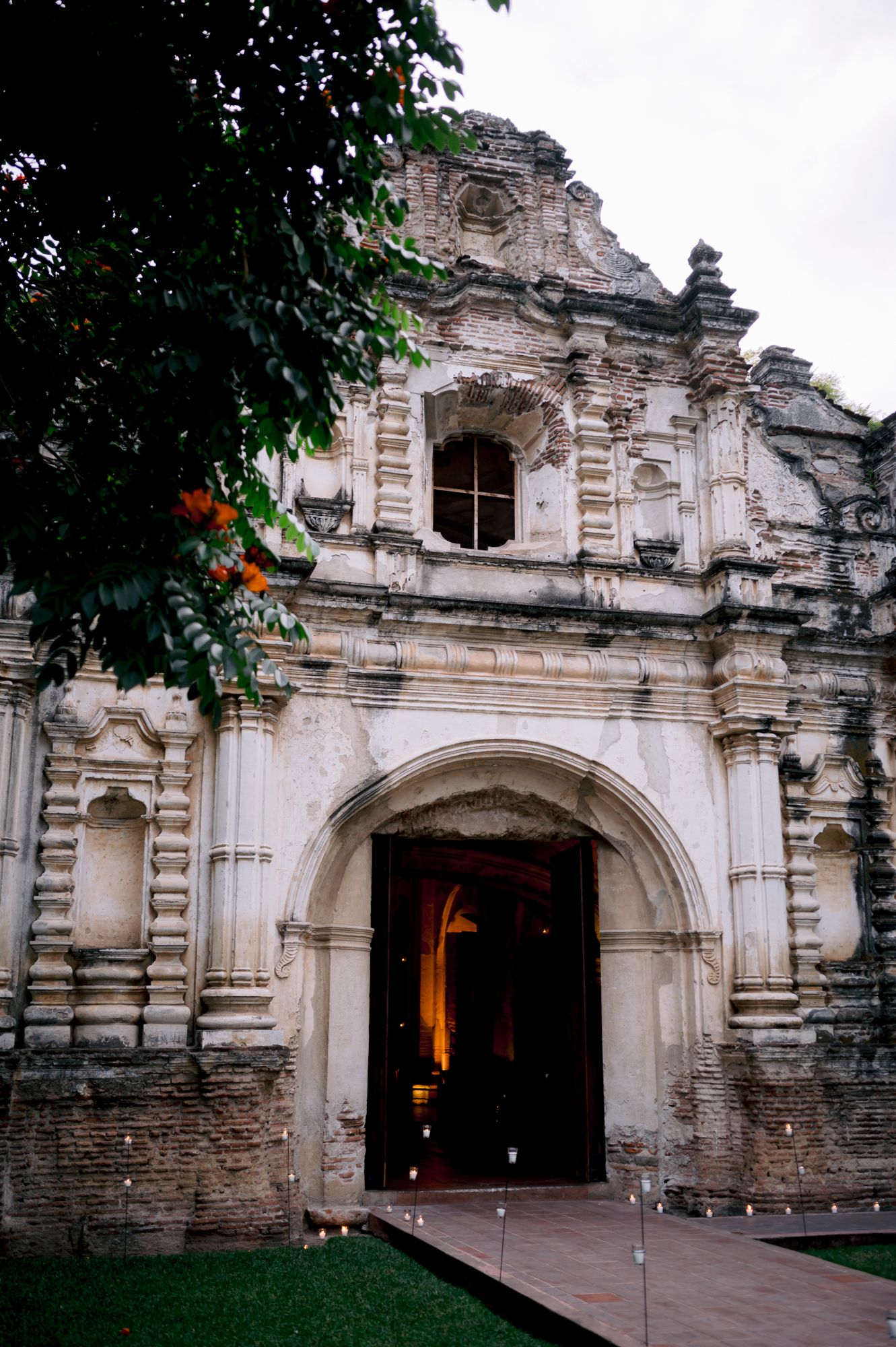 Ancient stone church facade with ornate baroque details and arched doorway surrounded by lush foliage.