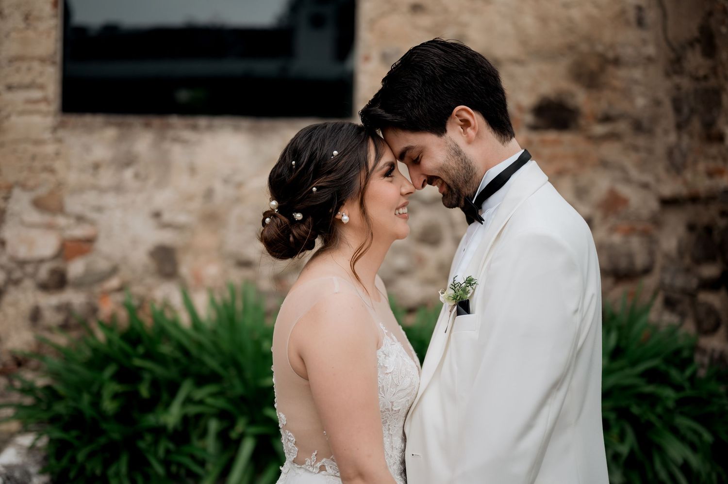 Tender forehead touch between bride and groom during outdoor wedding photoshoot.