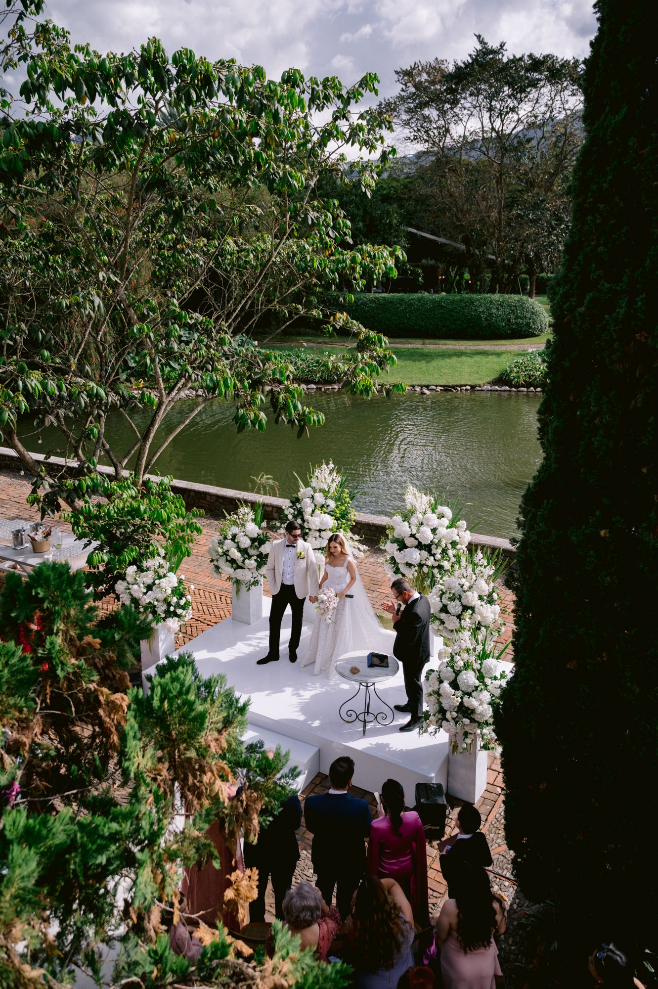 Outdoor lakeside wedding ceremony setup with white aisle runner and floral arrangements by the water.